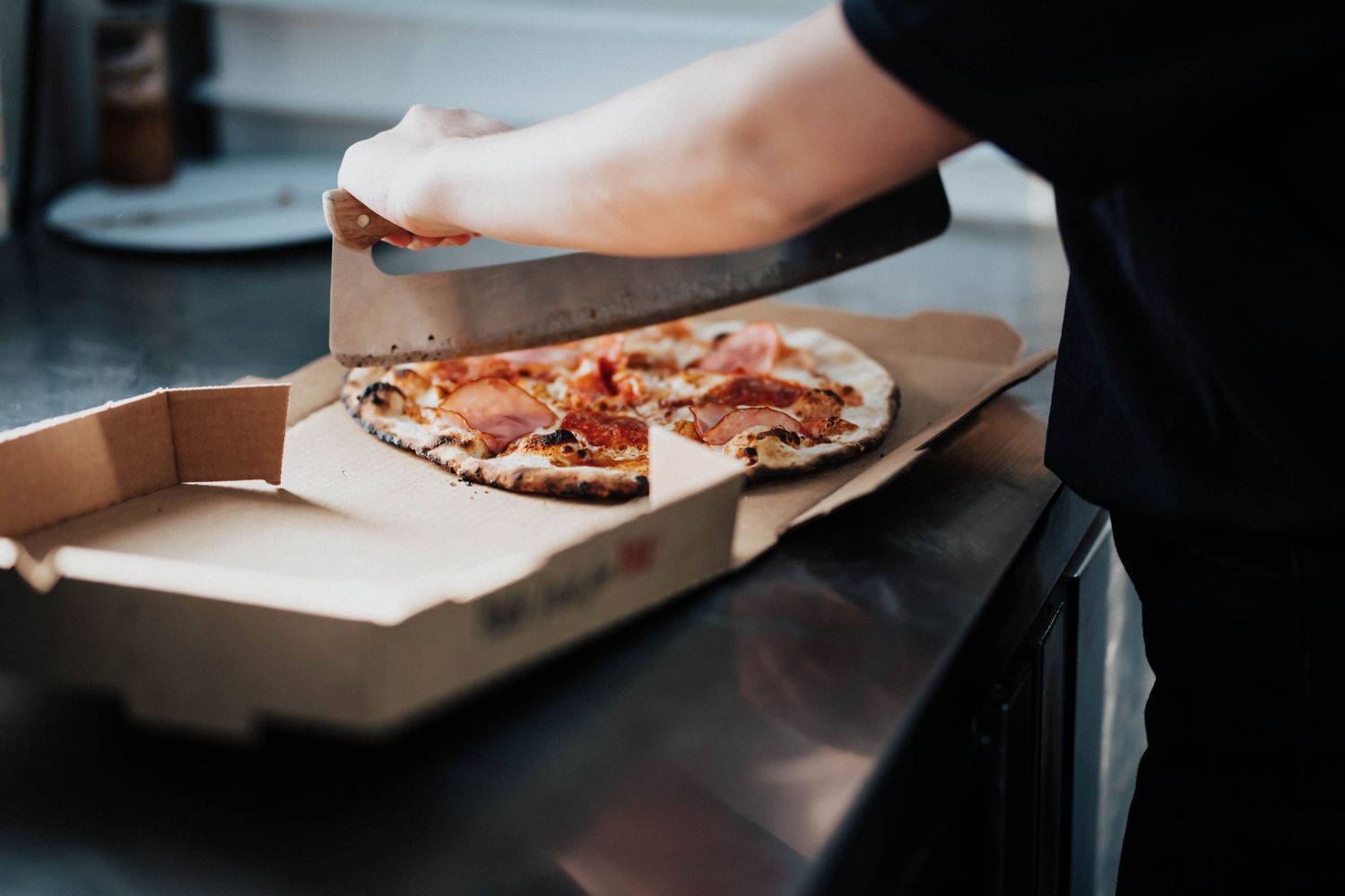 Chef placing a freshly made pepperoni pizza into a cardboard delivery box.