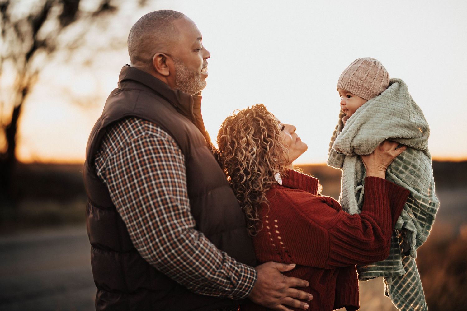 Grandparents holding grandchild together at sunset in outdoor portrait.