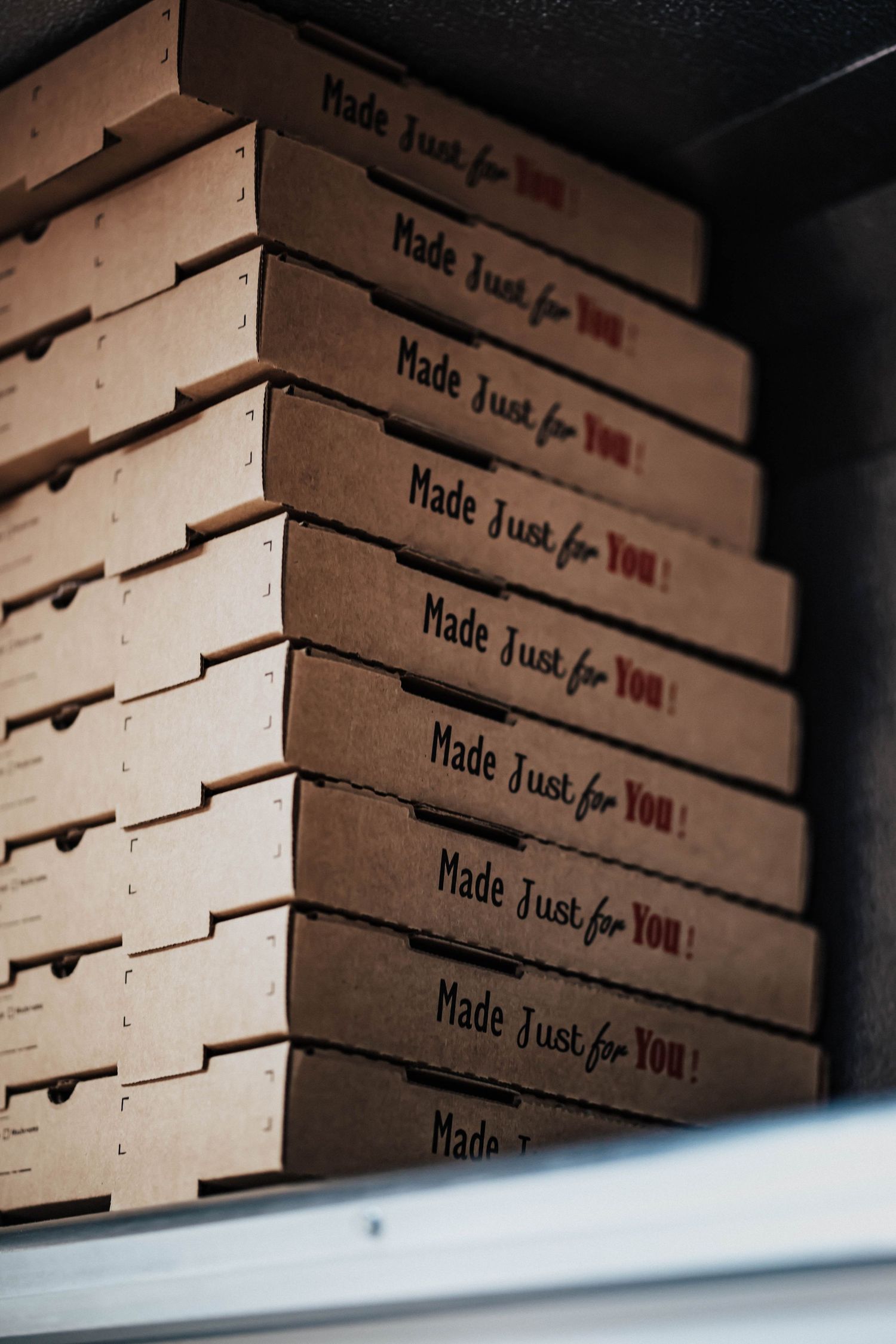 Stack of brown cardboard pizza boxes labeled Made Just for You on a shelf.