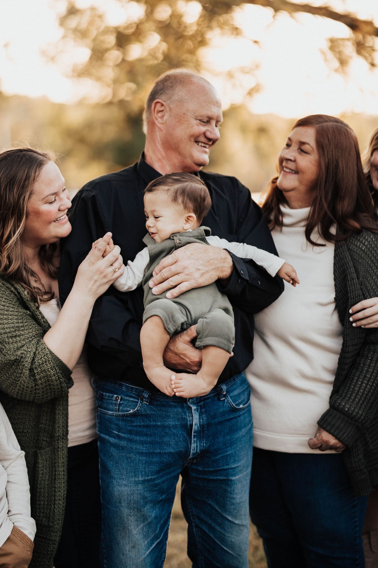 Multi-generational family laughing together while holding an infant in warm sunset light.