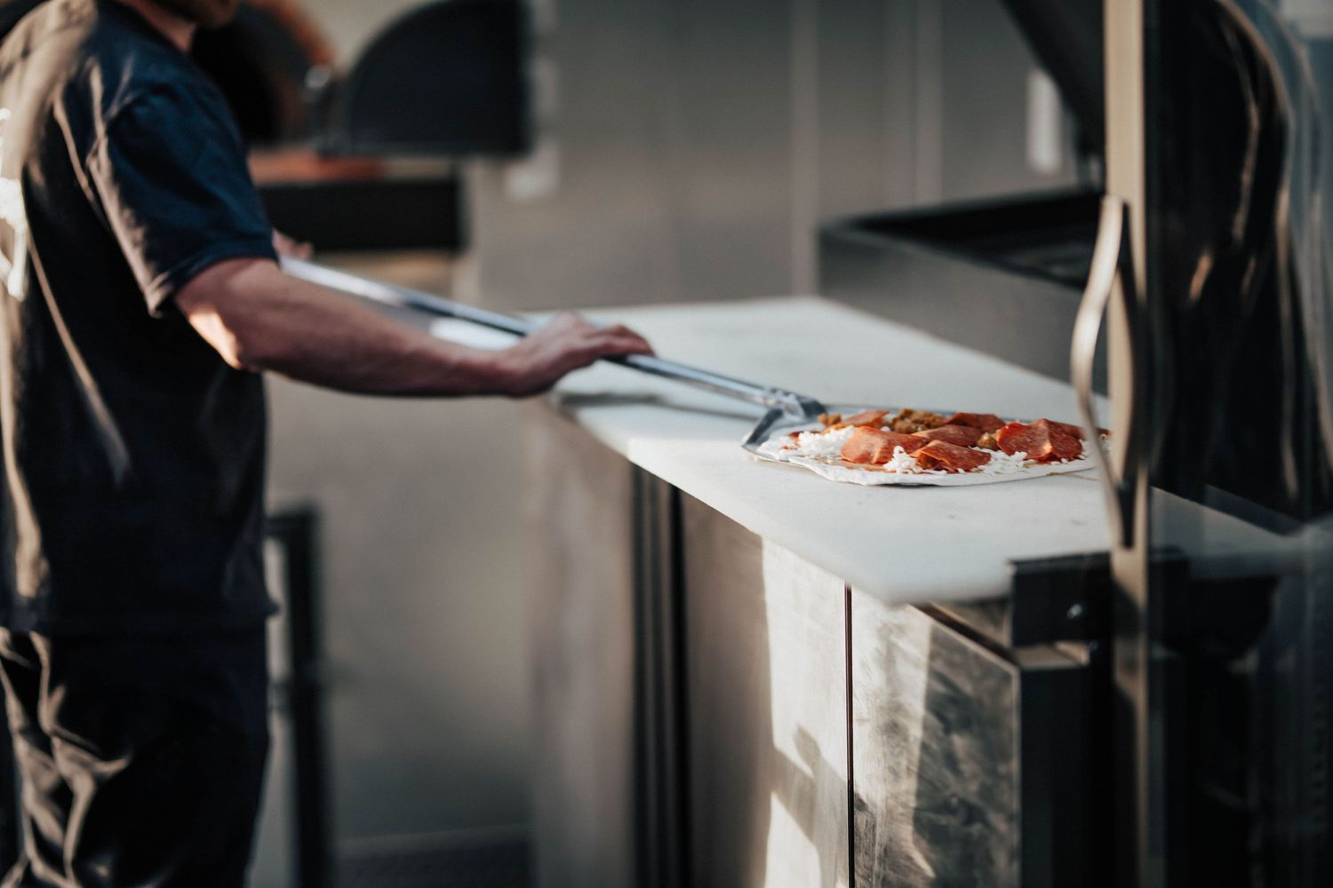 Pizza chef sliding a fresh pepperoni pizza into a professional wood-fired oven.