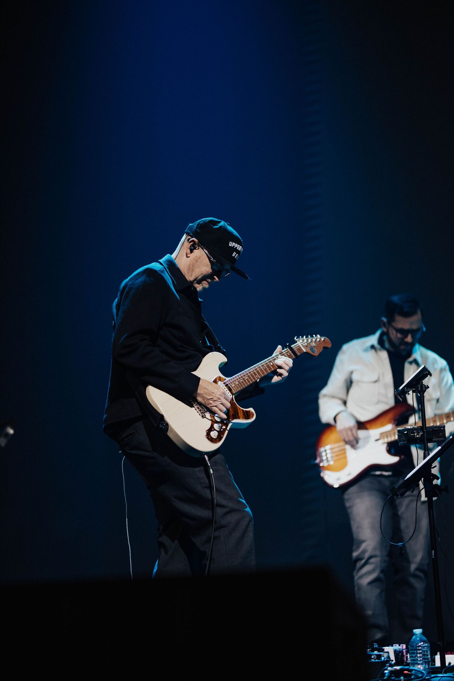 Guitarist in black cap performs on stage under blue spotlight at Creative Legacy Gathering 2025 concert.