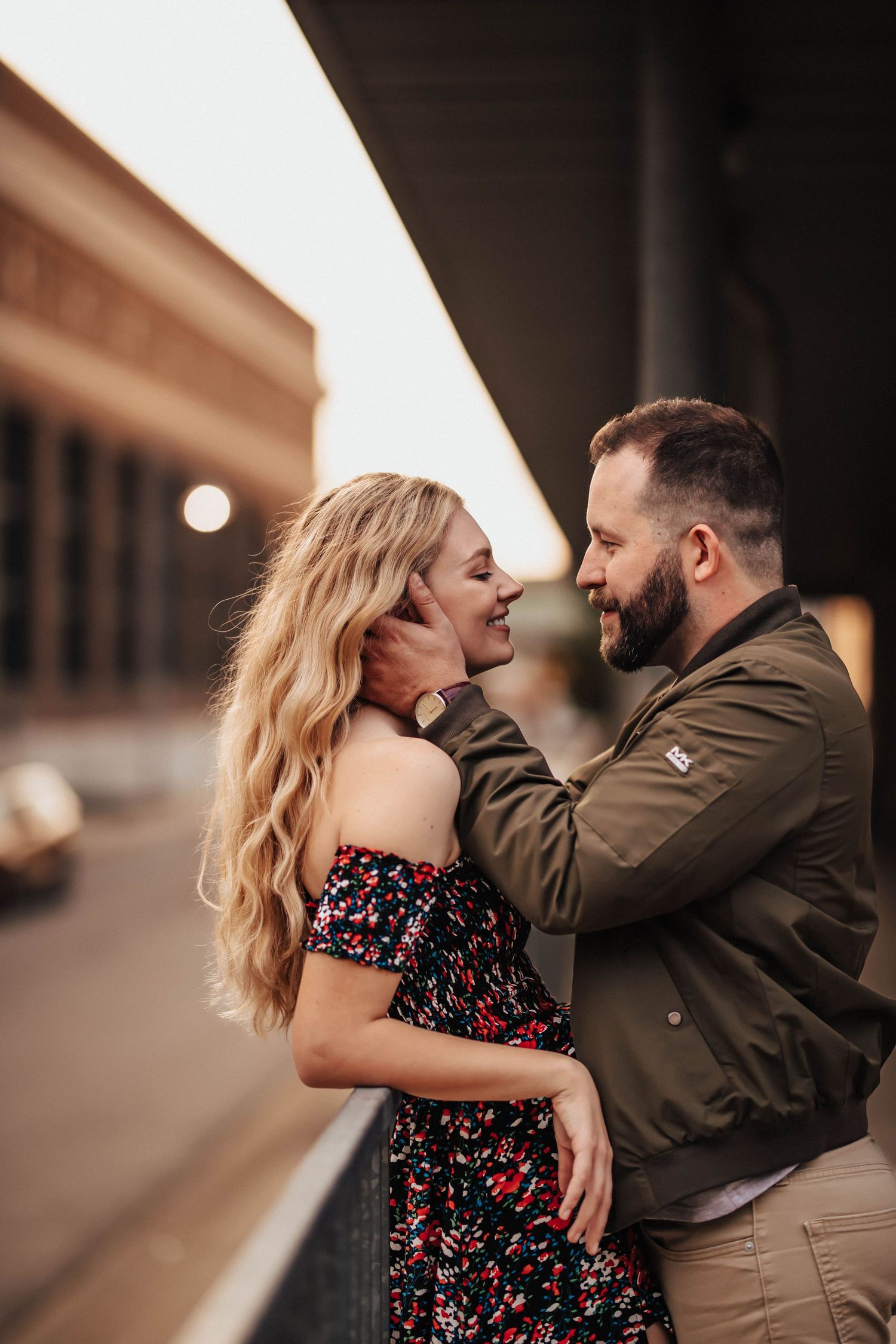 A couple shares a romantic embrace outdoors, the man tenderly holding the woman's face as they smile at each other.