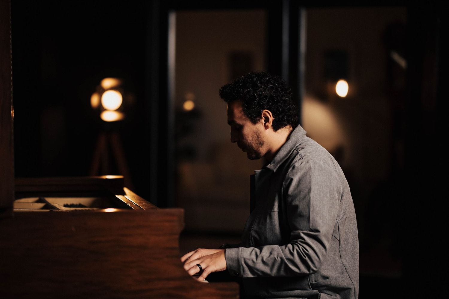 Man playing a grand piano in a dimly lit studio with warm spotlight ambiance.