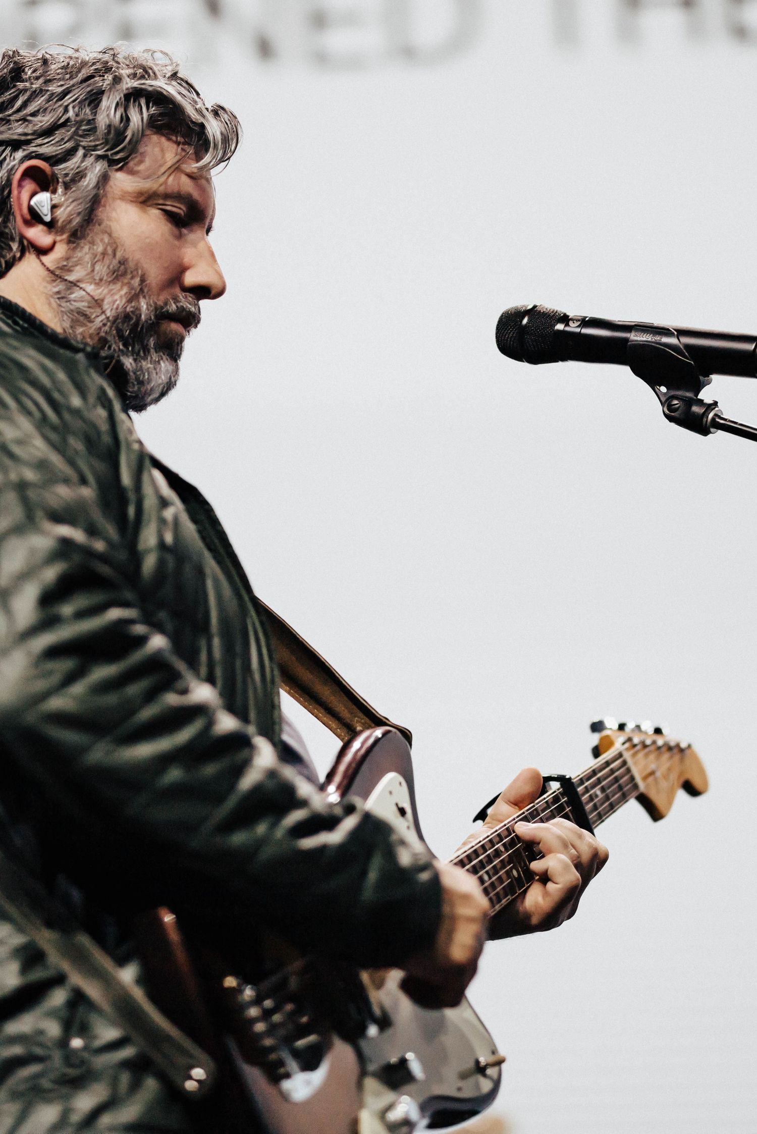 Close-up of bearded male guitarist playing electric guitar near a microphone during live performance.