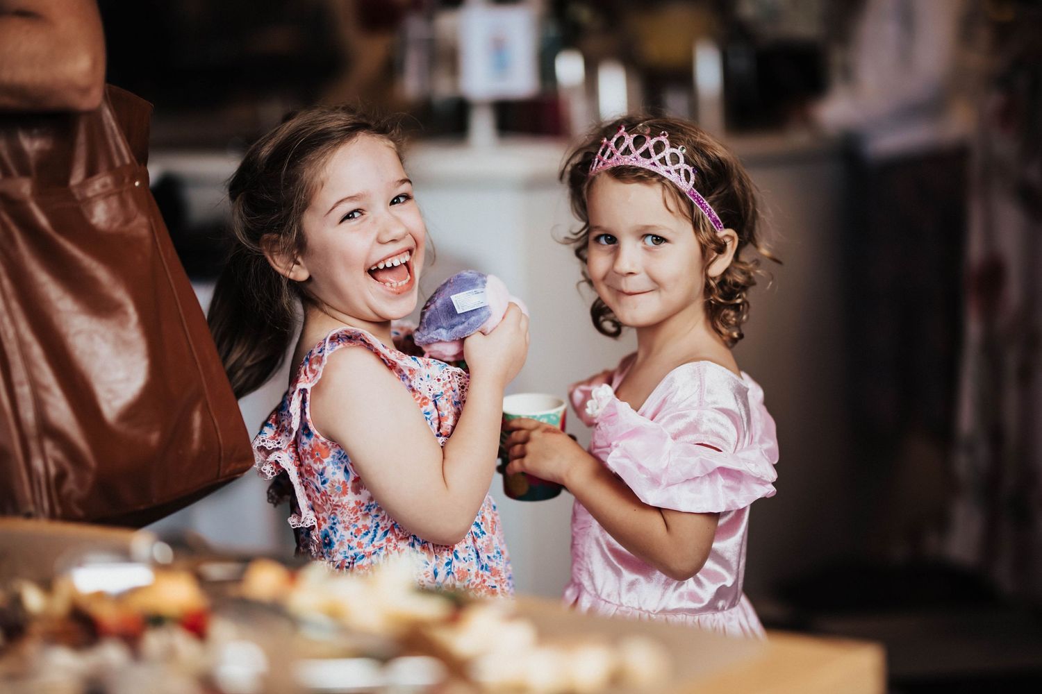 Two little girls in princess dresses laugh and eat cupcakes at a celebration party.