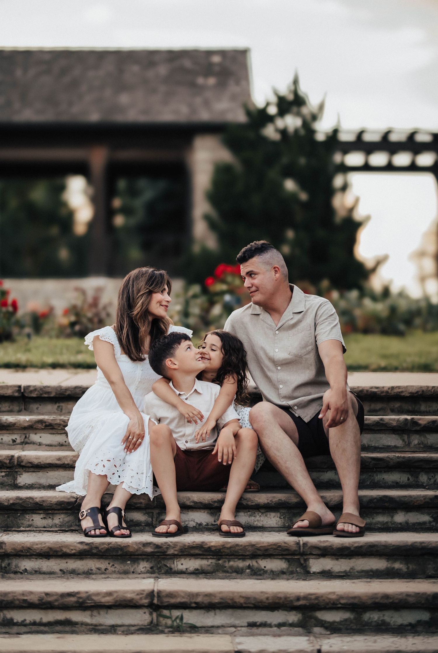 Family of four sitting on stone steps in a garden, sharing a warm and joyful moment together.
