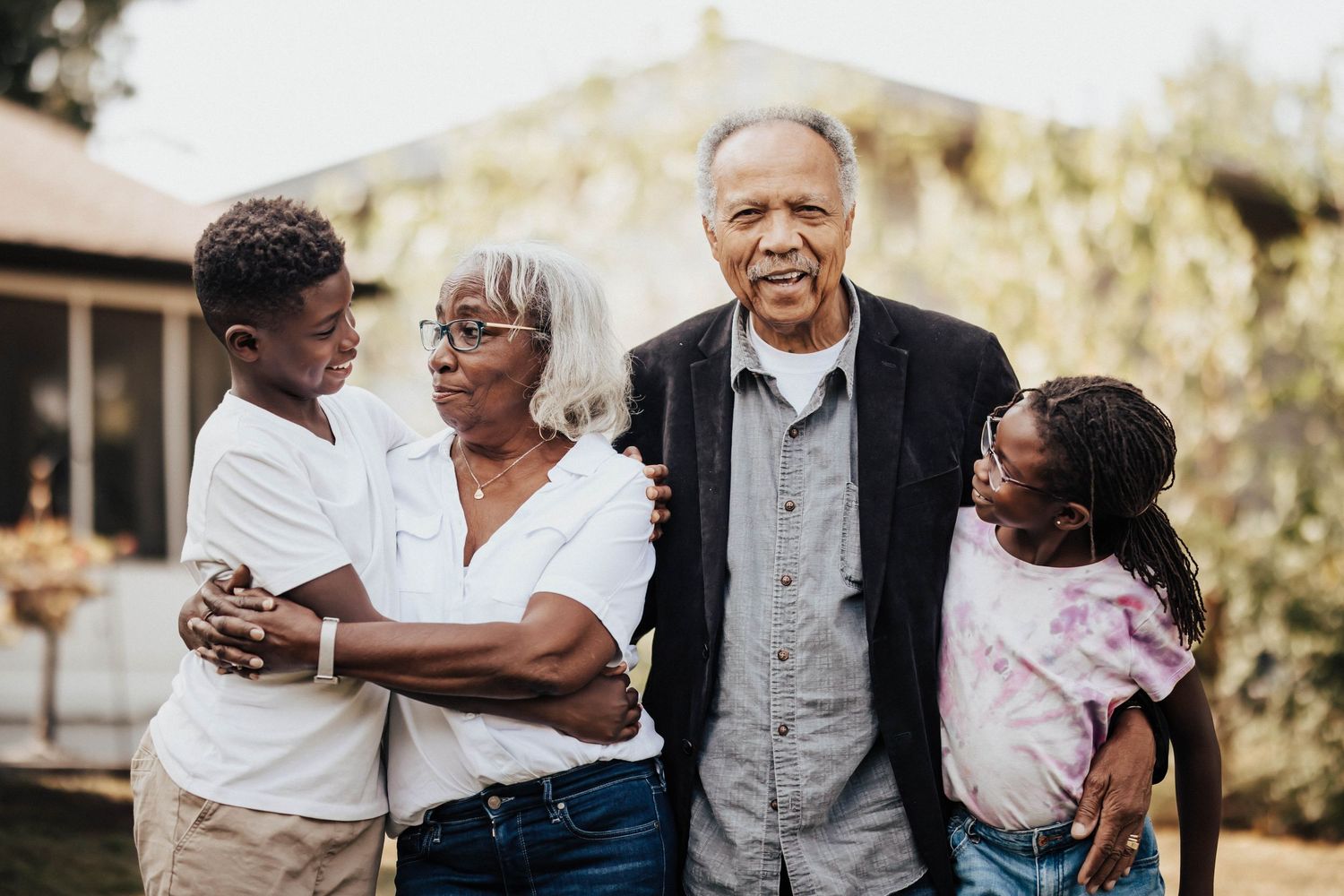 Grandparents hugging grandchildren outdoors in backyard family portrait.