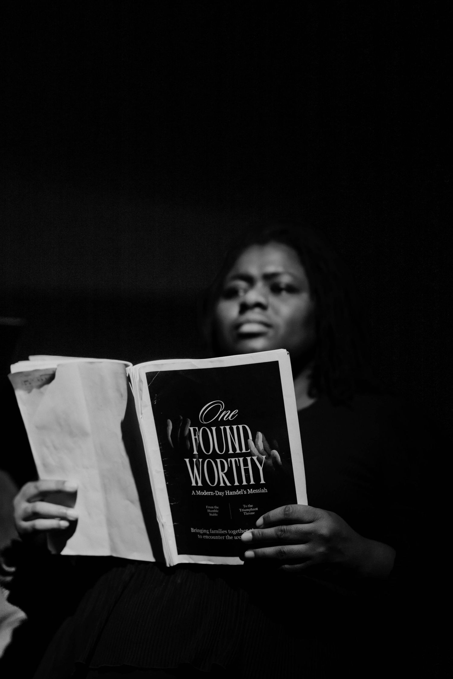 A person reads the book One Found Worthy, a Modern Day Handels Messiah, in a black and white photo.
