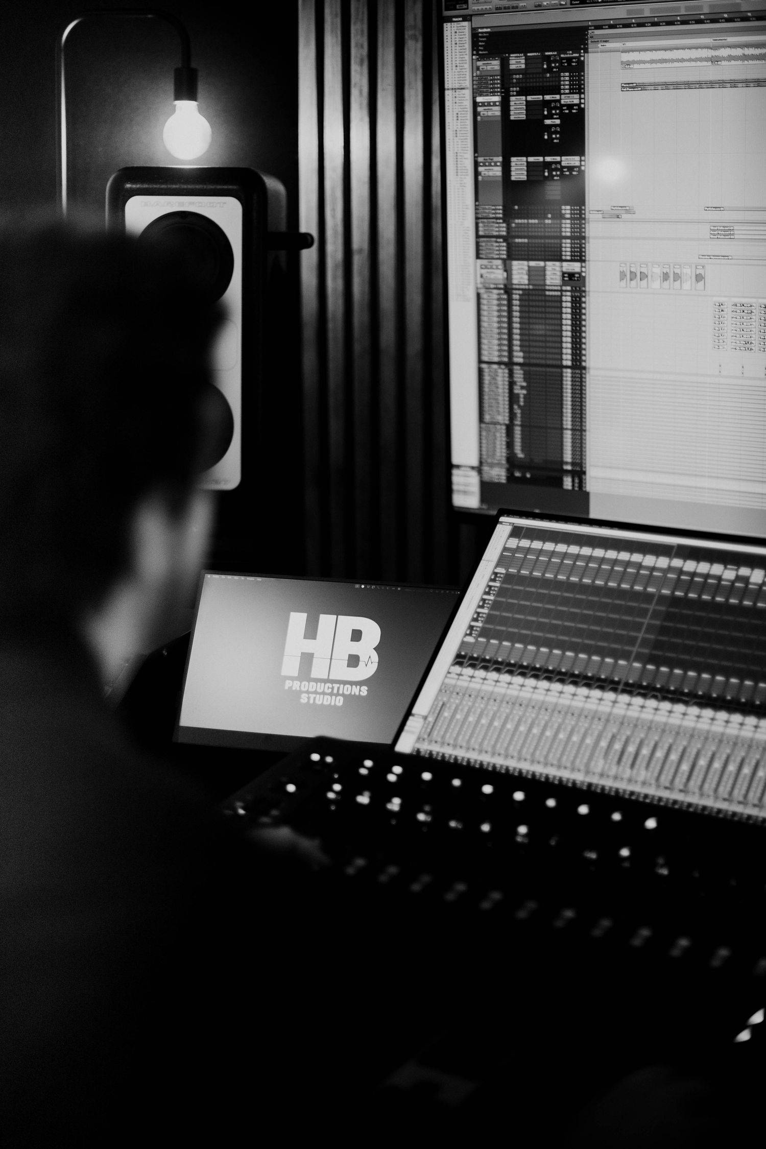 Black and white photo of a music producer working at HB Productions Studio mixing console with monitors.