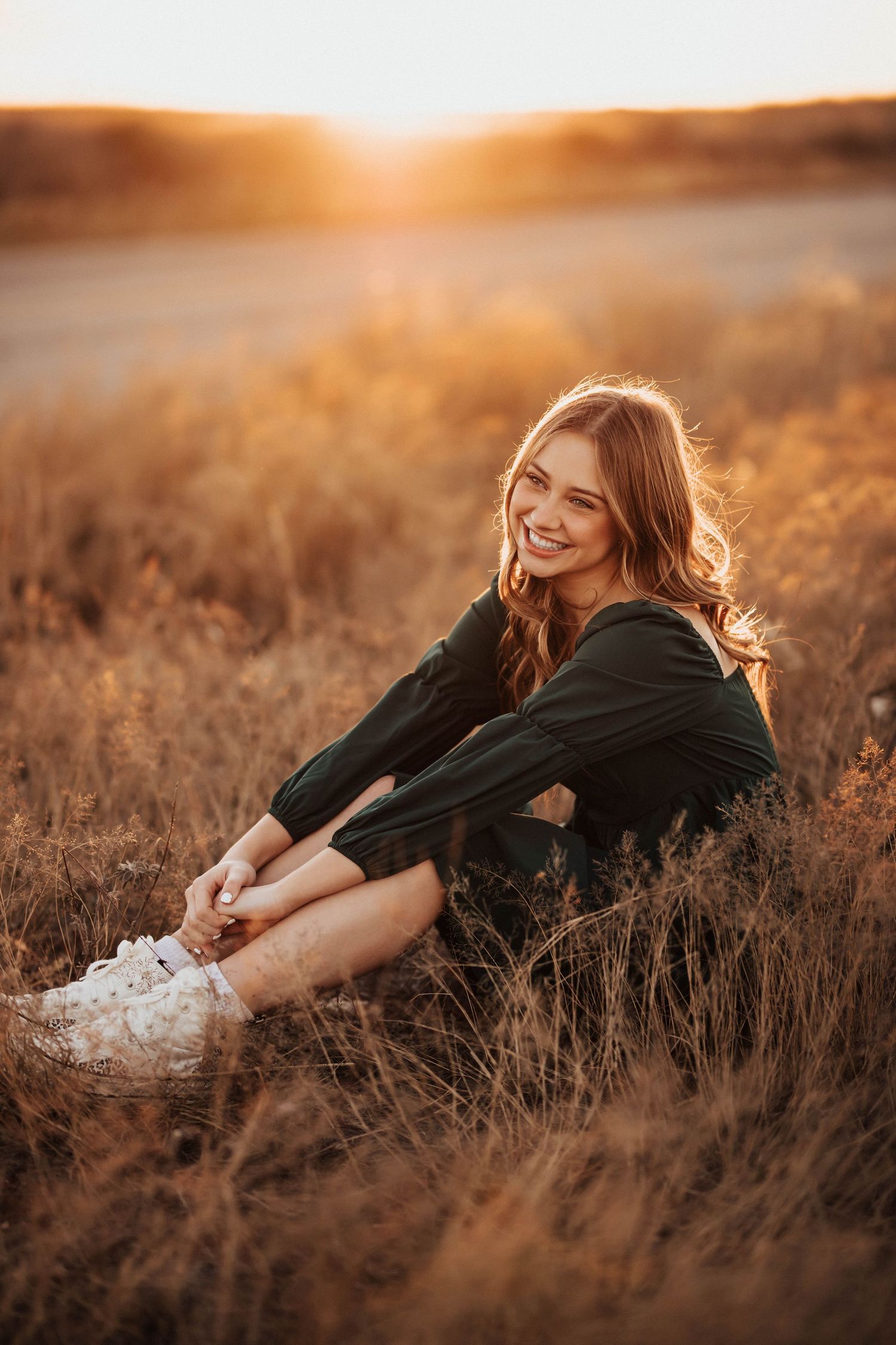 Smiling teenage girl sitting in golden field grass during beautiful sunset portrait session.
