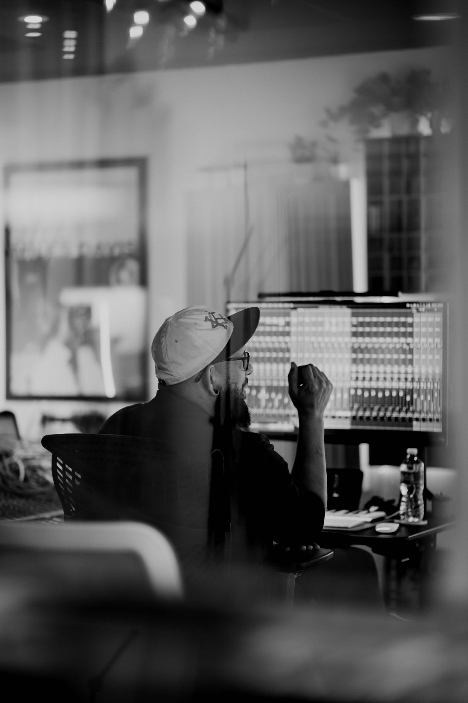 Black and white photo of a person wearing a cap working at a large mixing console in a recording studio.