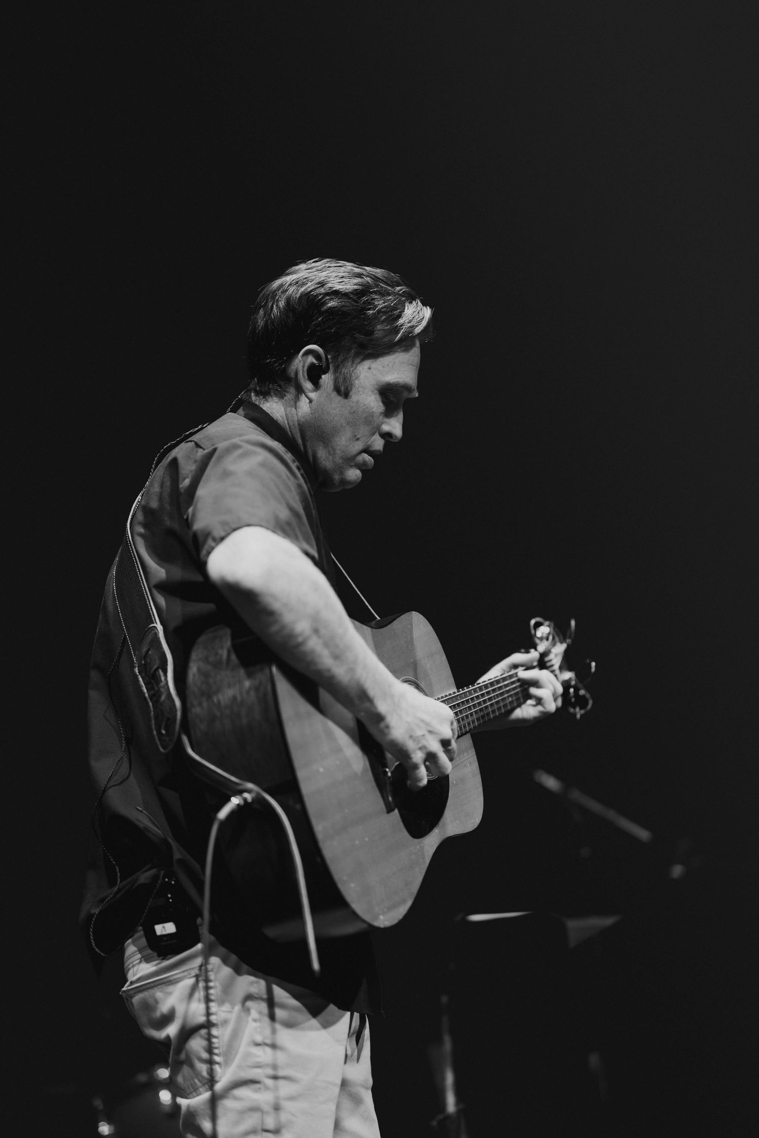 Black and white photo of a man playing acoustic guitar on a dark concert stage.
