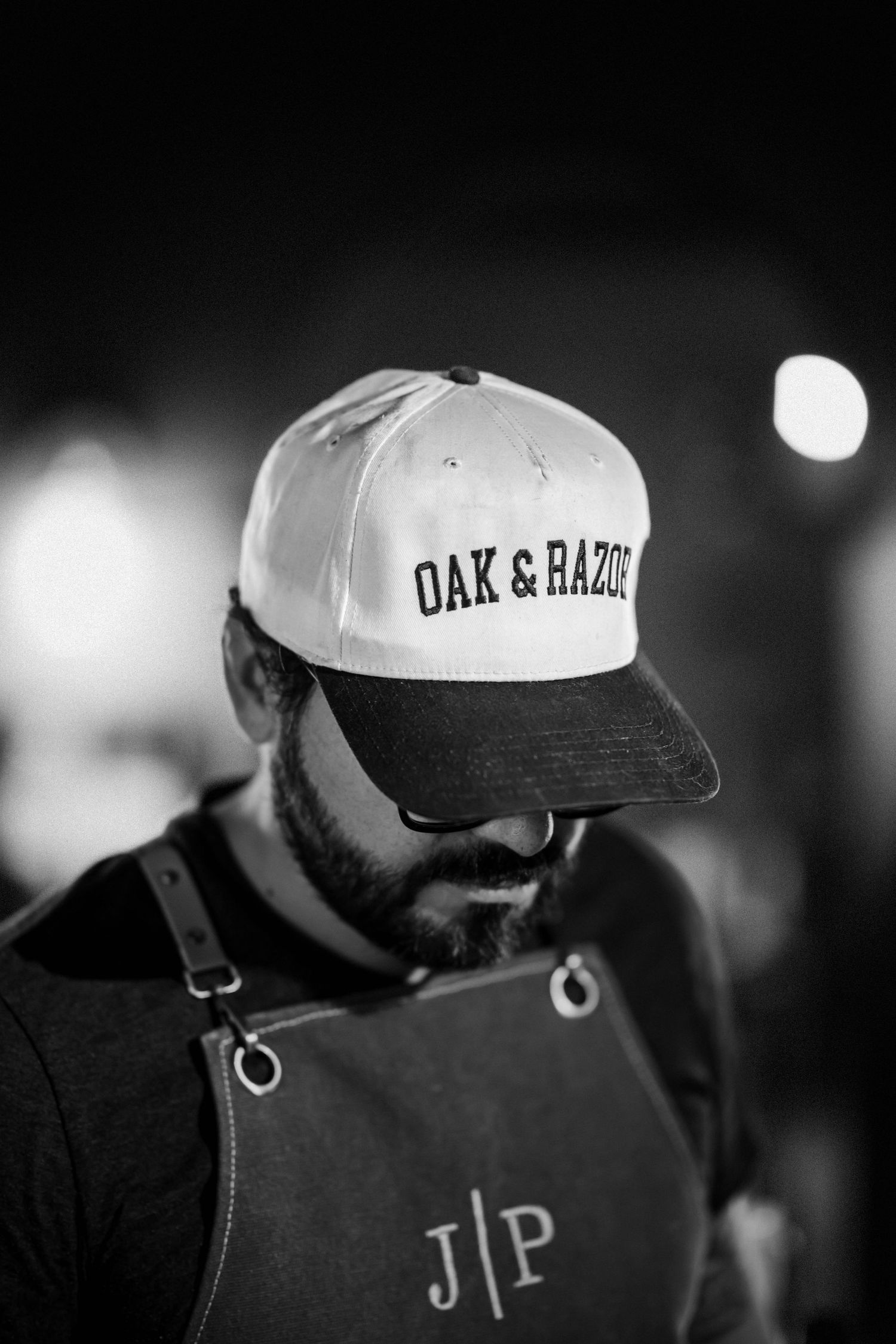 Black and white portrait of bearded man wearing Oak and Razor cap and JP monogrammed apron.