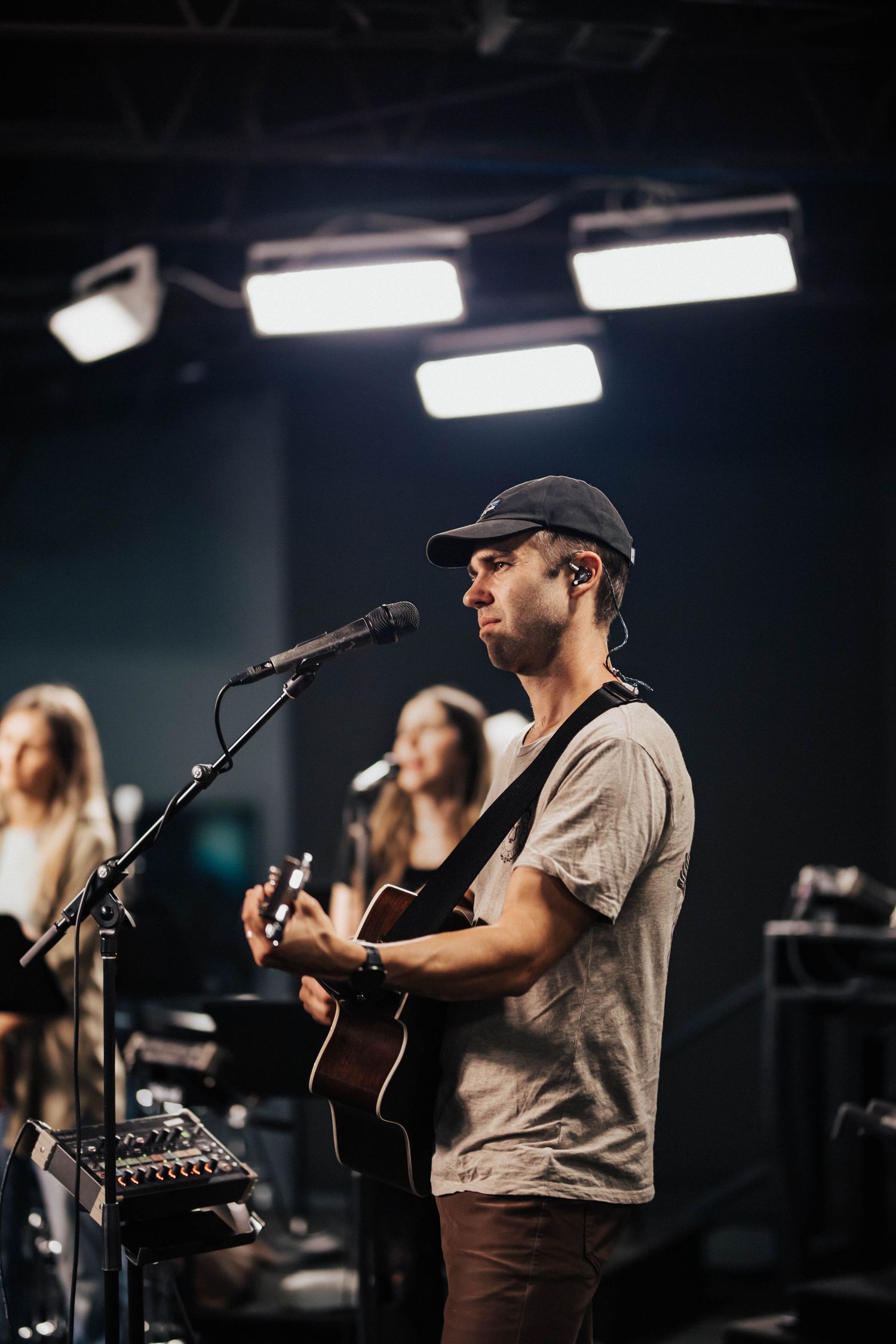 Male guitarist in cap performs at microphone during contemporary church worship service.