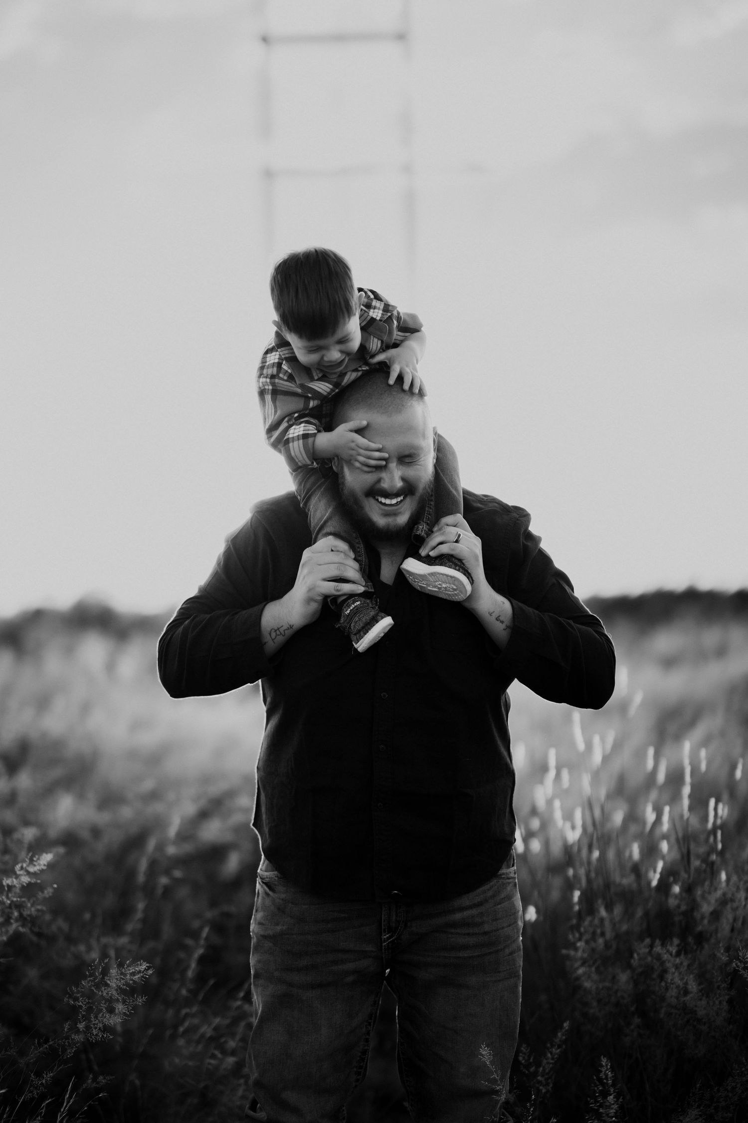 Black and white photo of a laughing man carrying a young boy on his shoulders in a field.