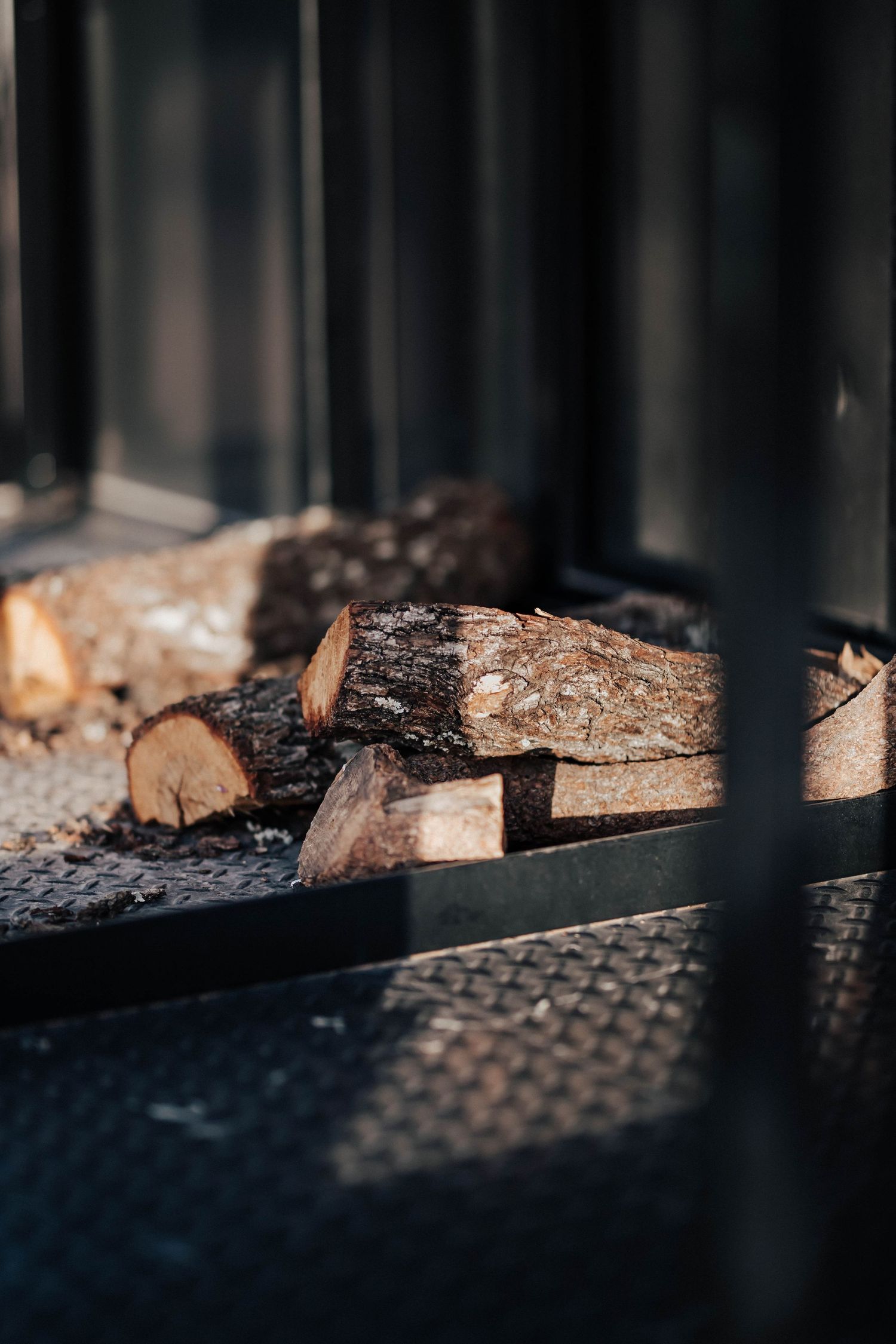 Split firewood logs stacked inside a dark metal wood-fired pizza oven compartment.