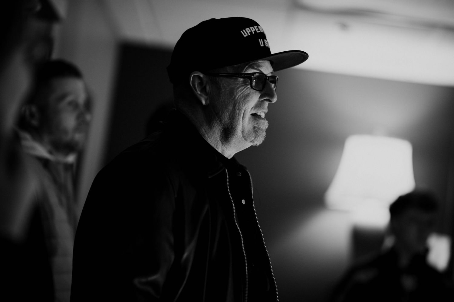 Man in black cap and glasses speaking at Creative Legacy Gathering 2025 event in dramatic black and white photo.