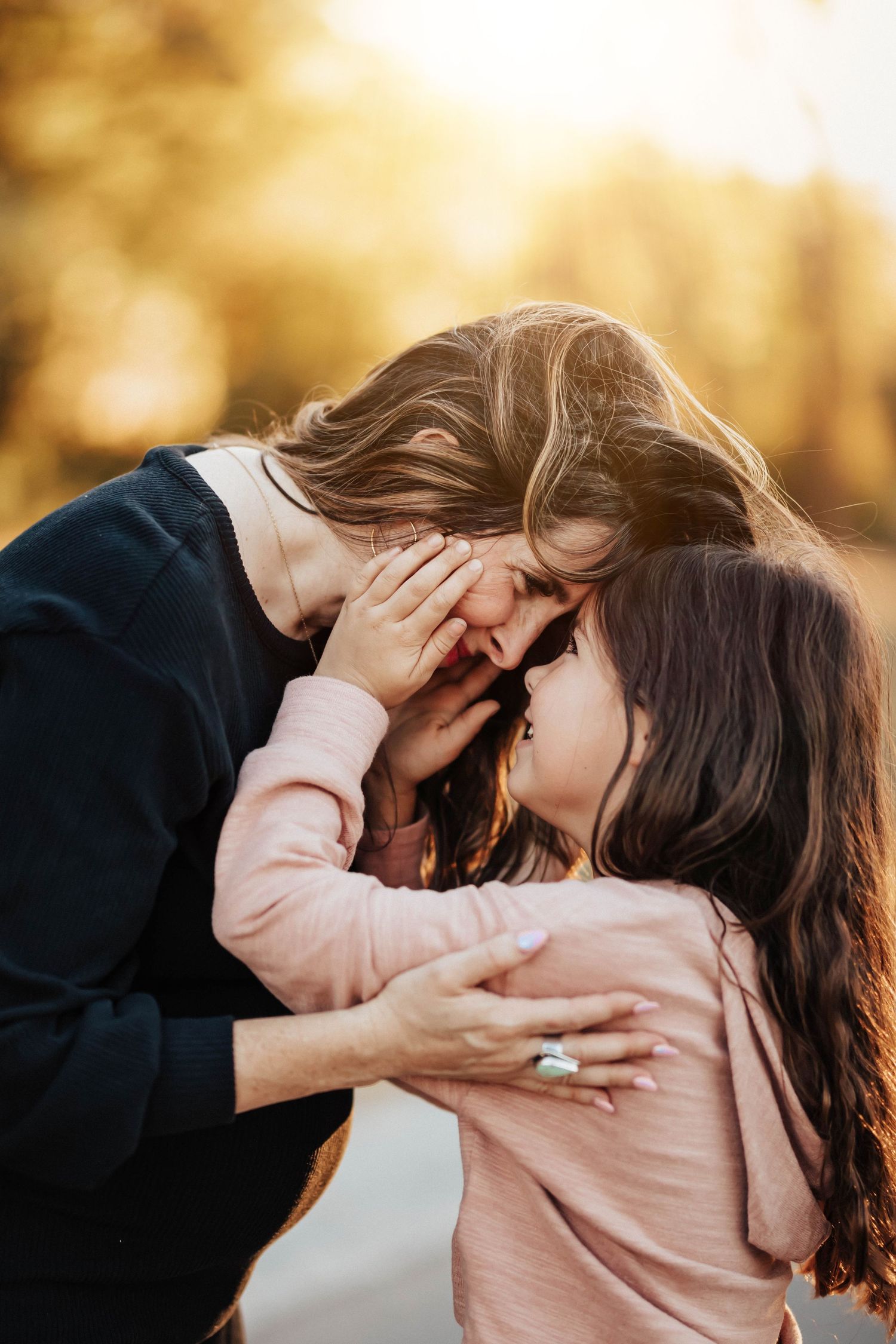 A mother and daughter share a tender forehead-to-forehead embrace in golden sunset light.