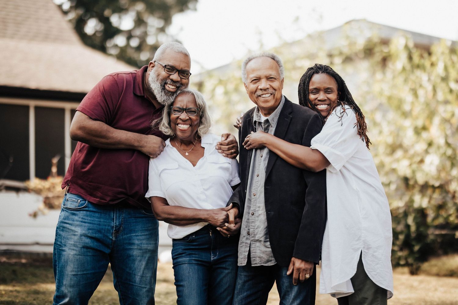 Four adults smiling and embracing in a joyful outdoor family portrait.