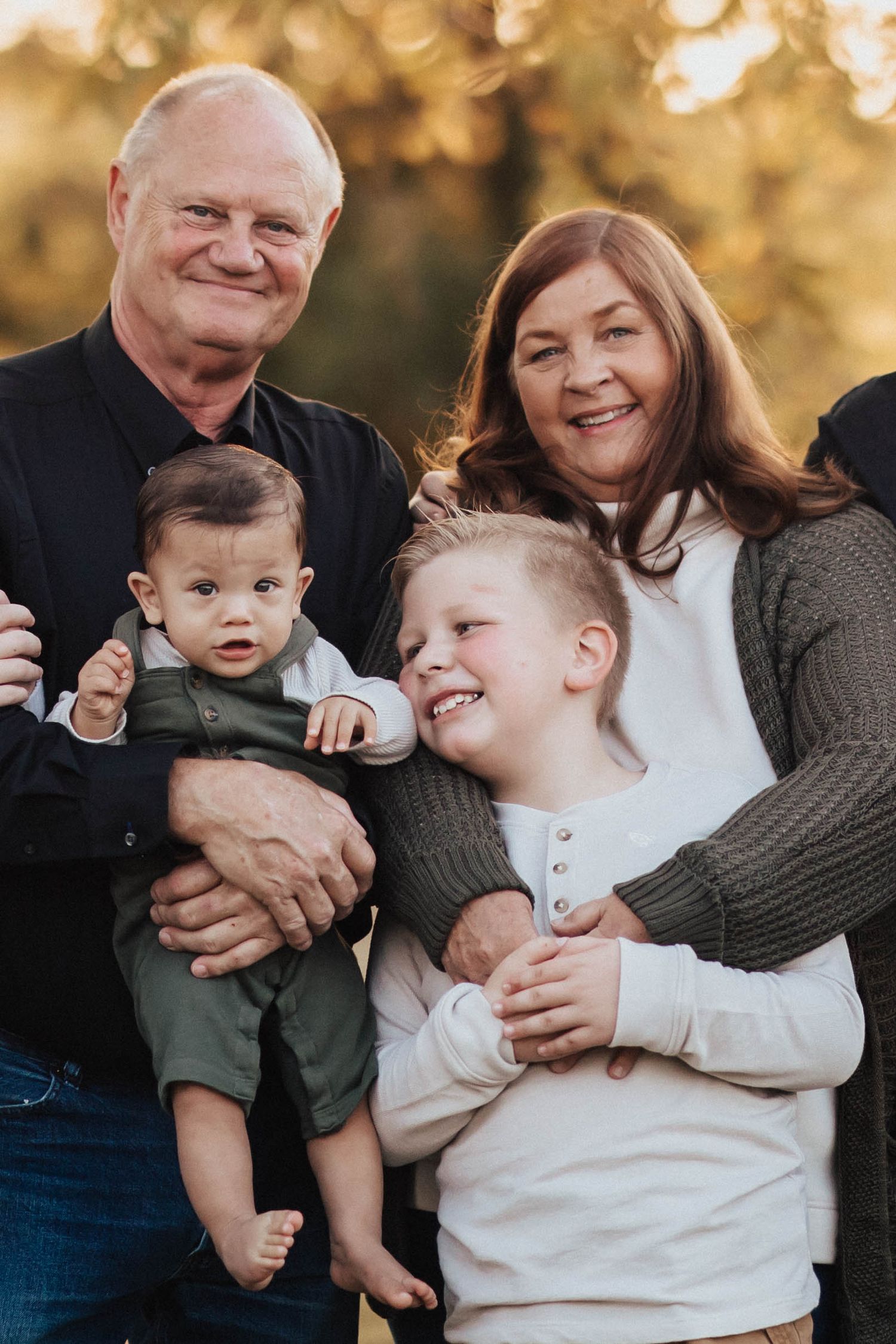 Grandparents holding a baby and young boy, smiling warmly in golden outdoor light.