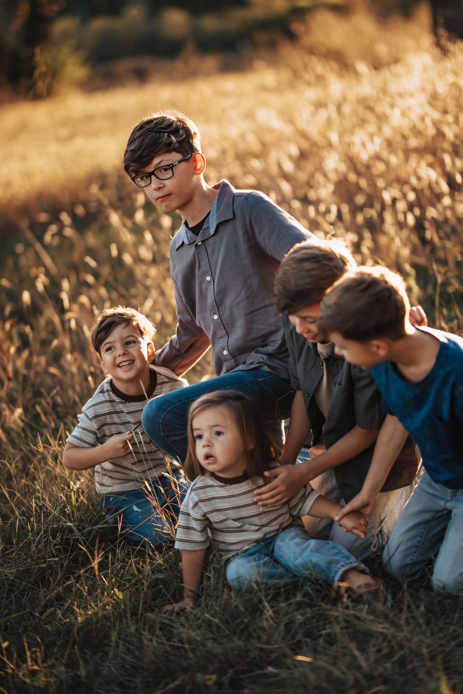 Four brothers sitting together in a sunlit golden grass field at sunset.