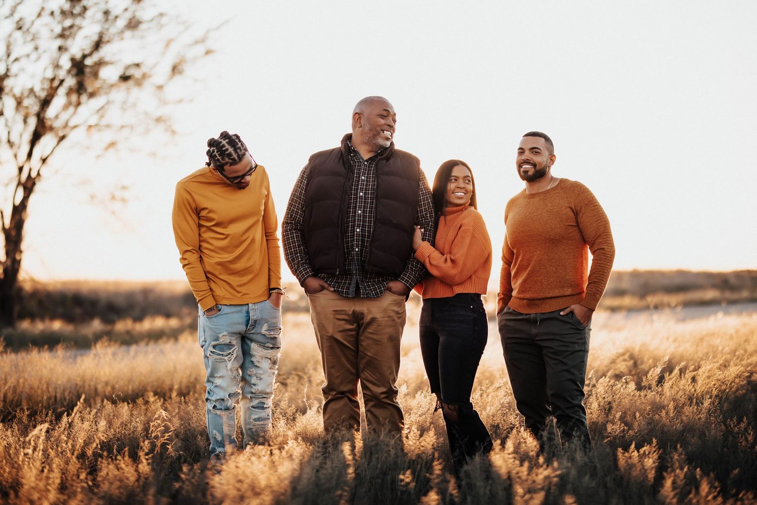 Family of four standing in golden field at sunset wearing warm tones.