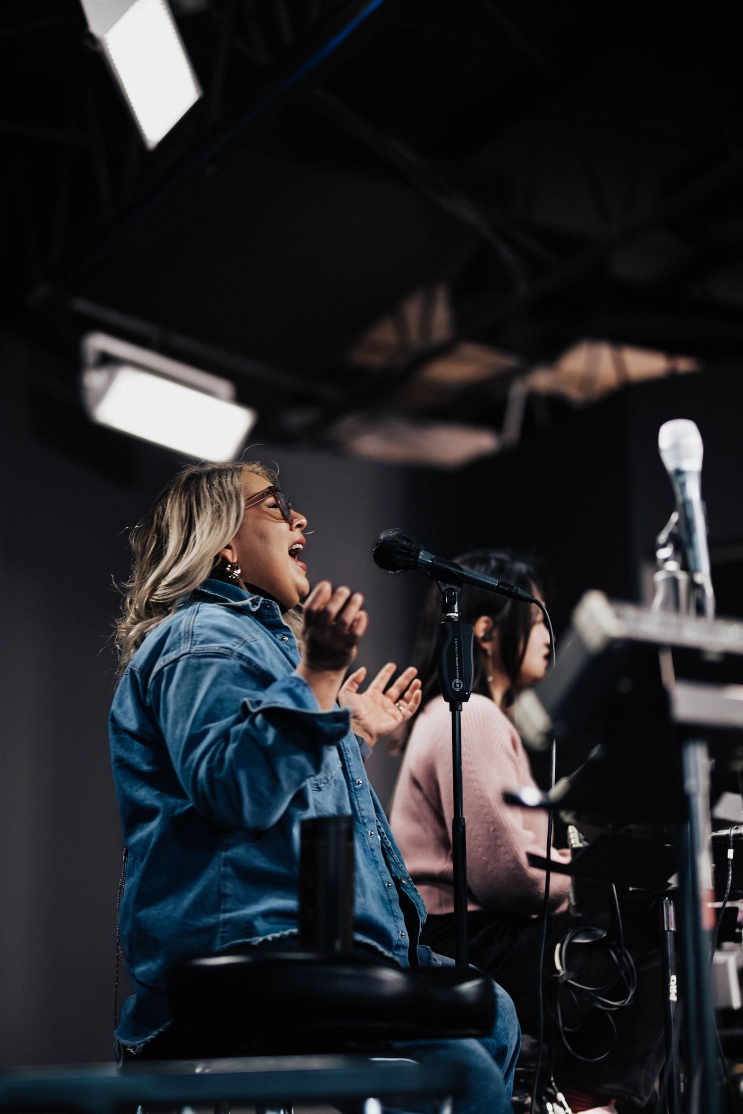 A blonde woman sings passionately into a microphone on stage during a worship session.