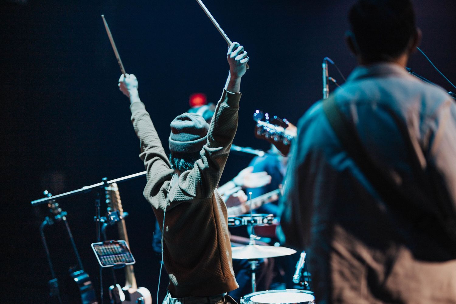 Energetic drummer raising drumsticks in the air during a live concert performance on stage.