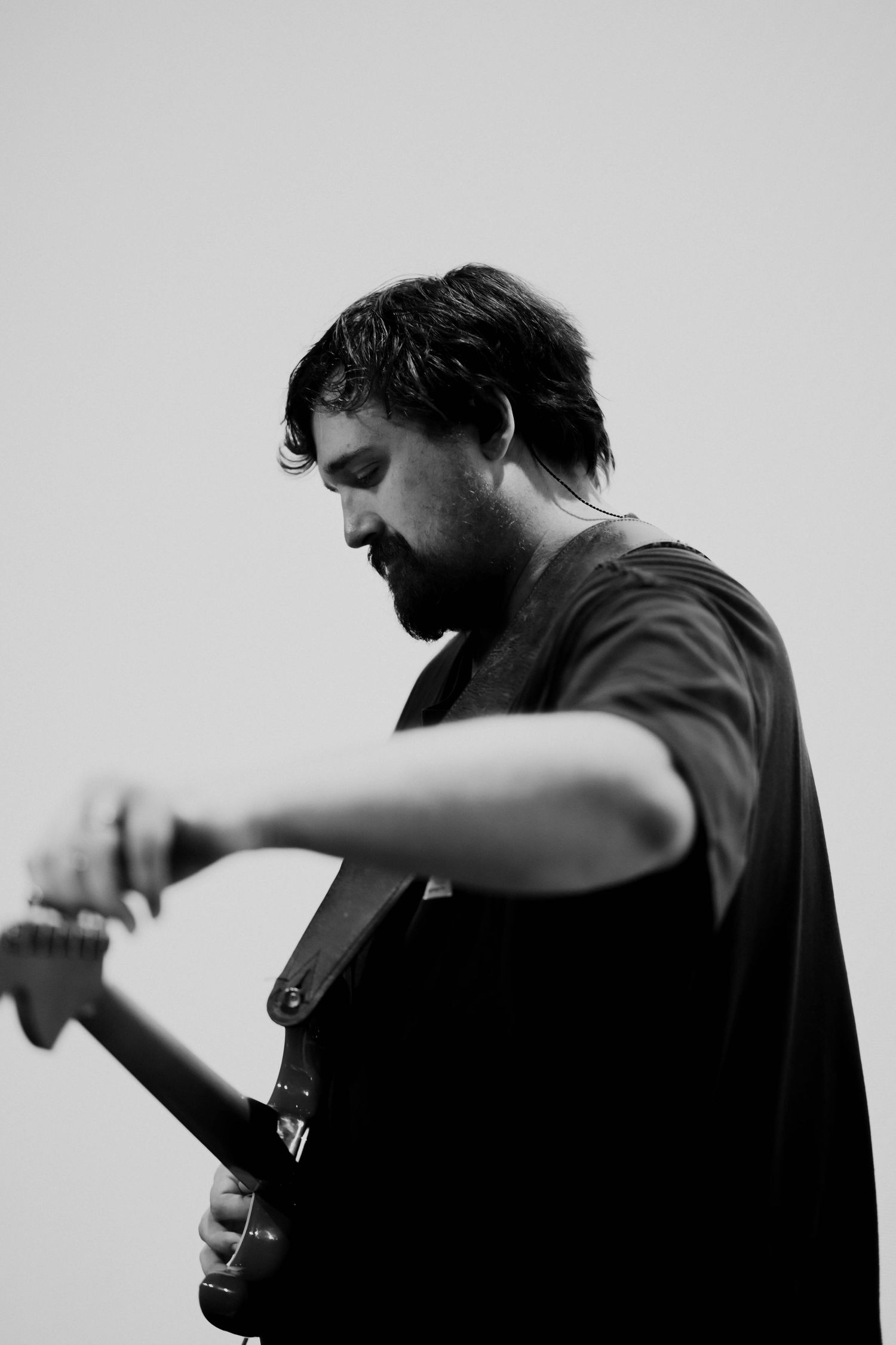 Black and white portrait of a bearded male guitarist playing electric guitar on stage.