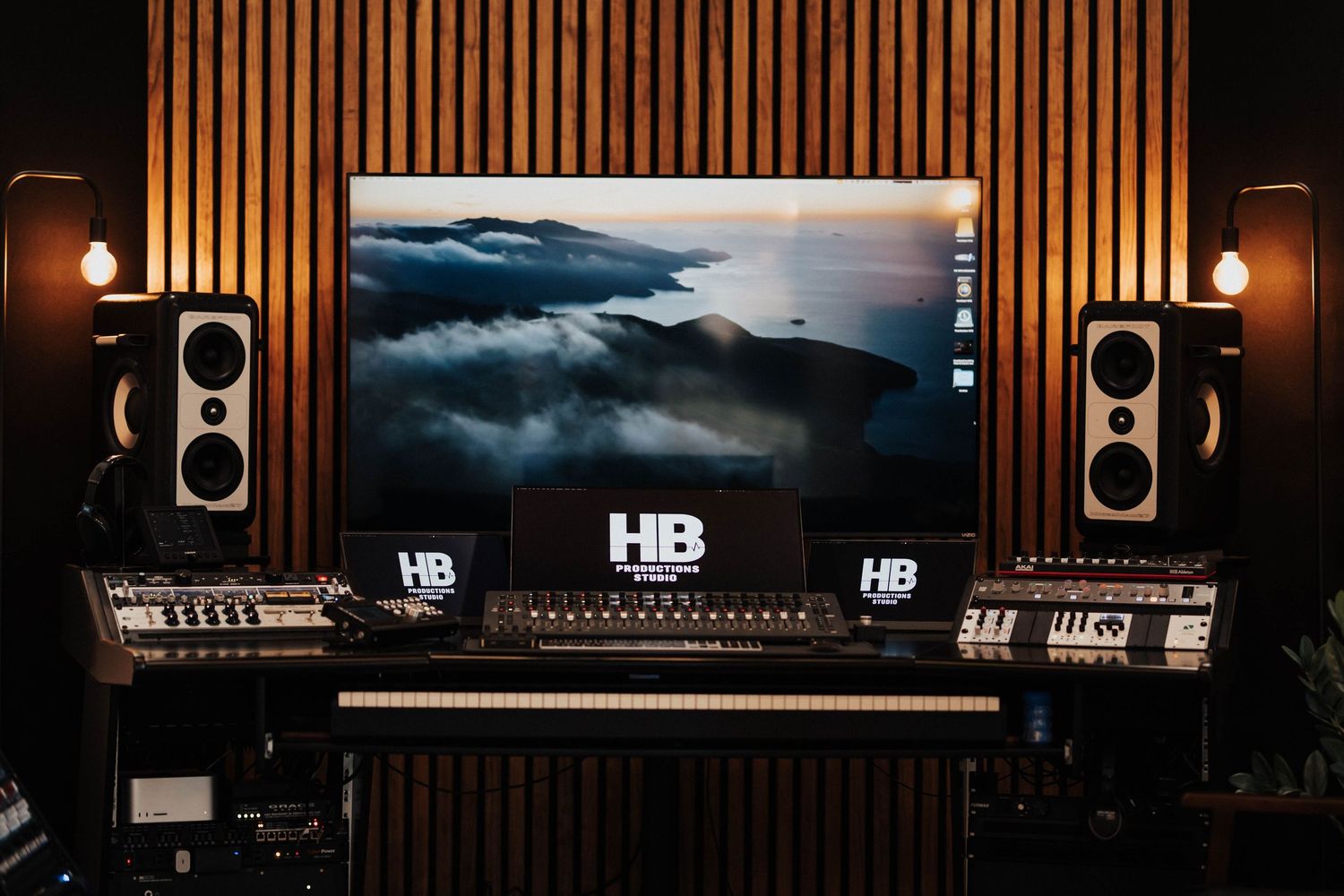 Professional recording studio with HB branding, mixing desk, monitors, and mountain landscape screen.