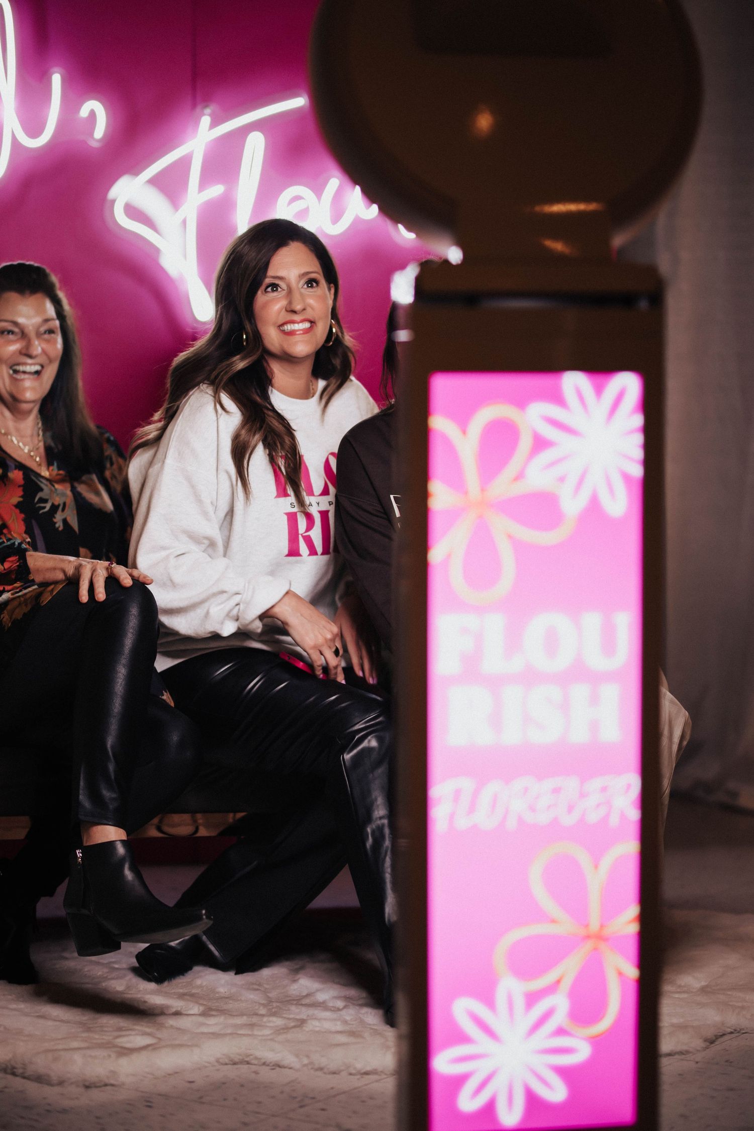 Two women sit together smiling near a Flourish photo booth at an event.