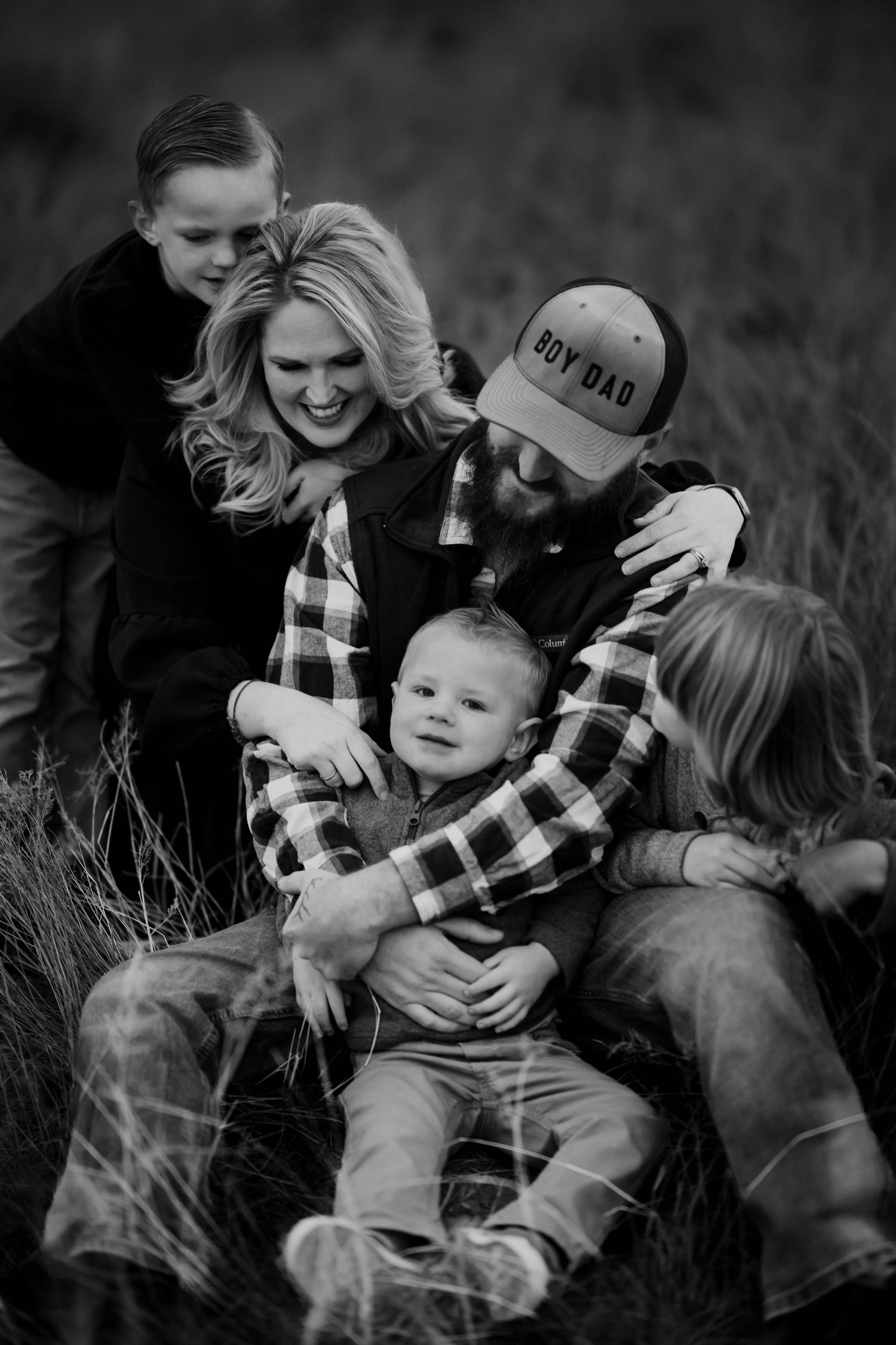 Black and white family portrait of parents and three children laughing in a field.