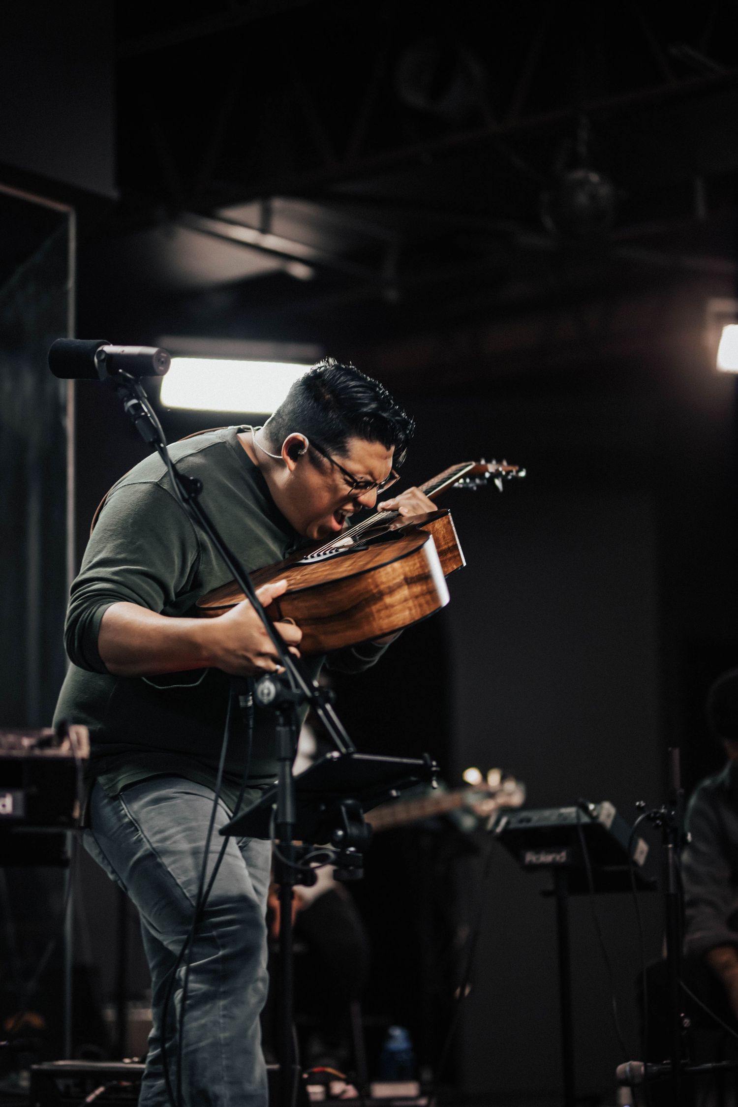 Musician passionately playing acoustic guitar on a dark studio stage under bright lights.
