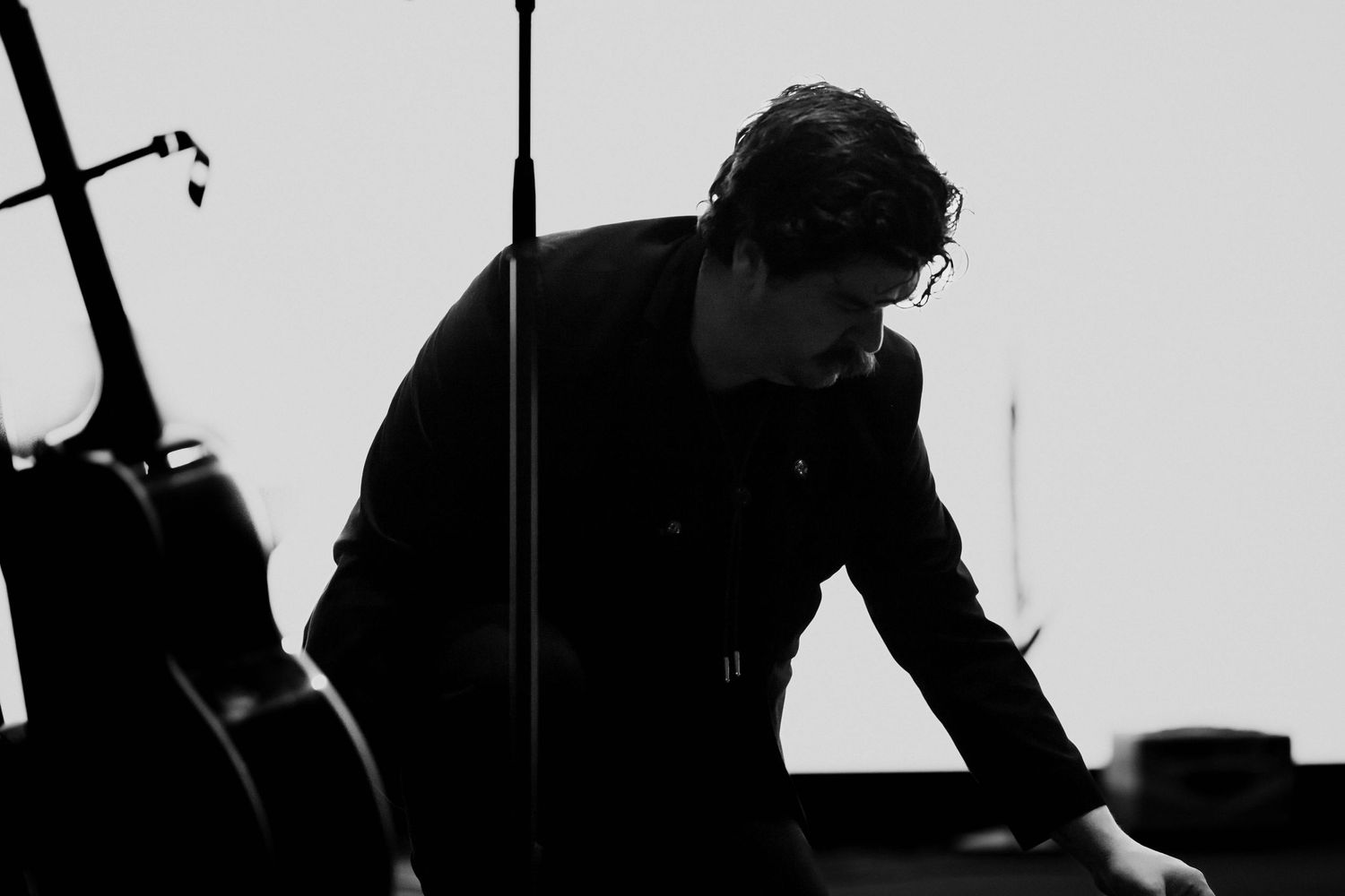 Black and white photo of a musician leaning over equipment on stage.
