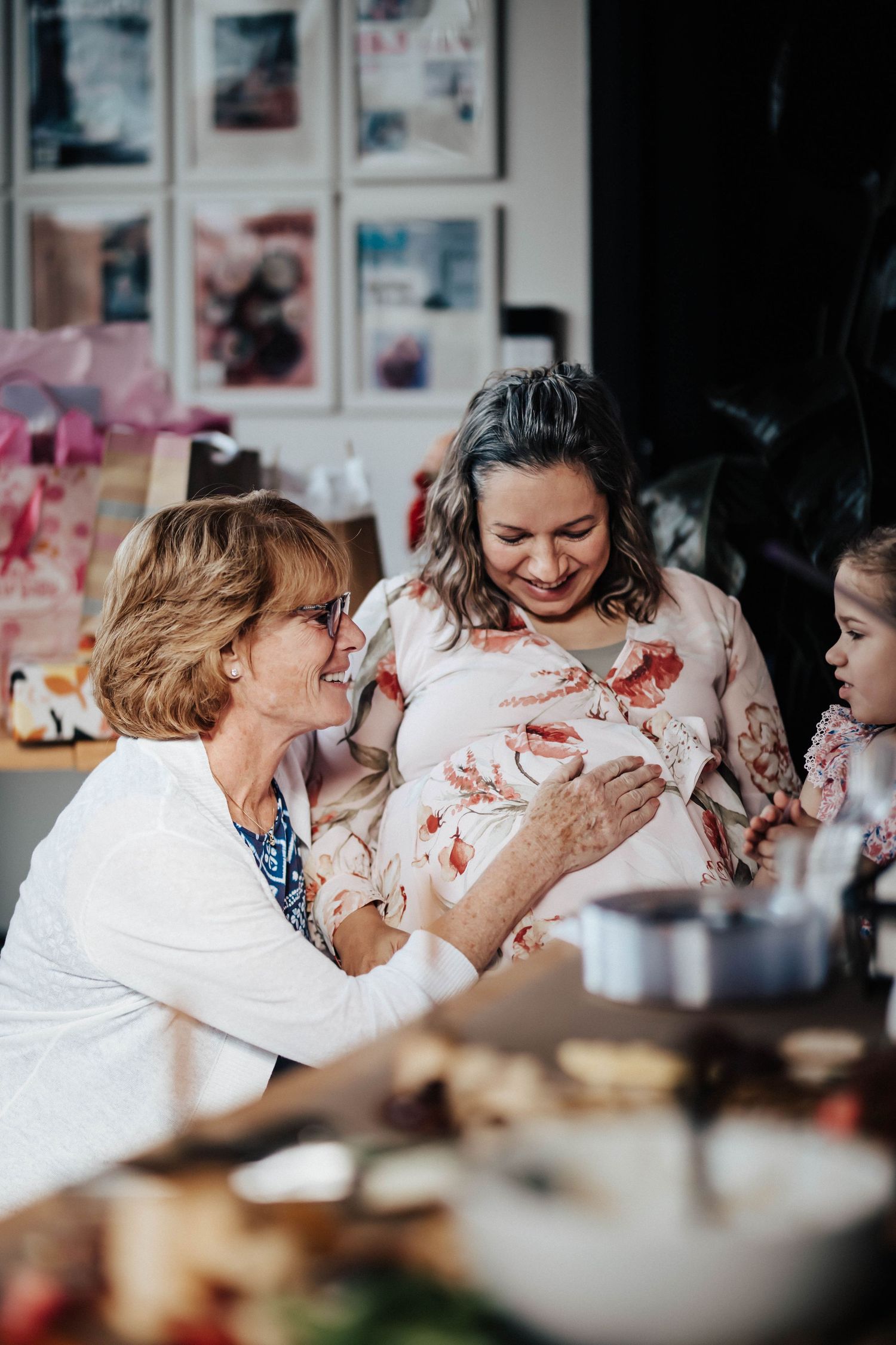Older woman touches pregnant belly while smiling with expectant mother and child at party.