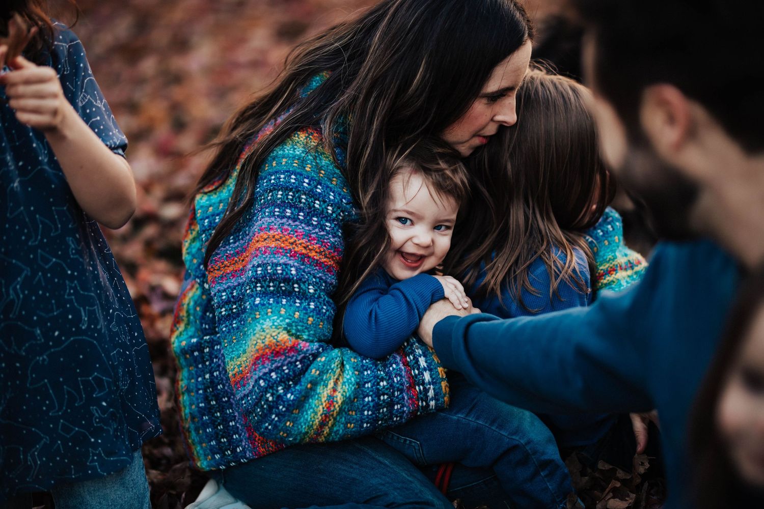 Mother in colorful sweater lovingly embracing her smiling toddler outdoors in autumn.