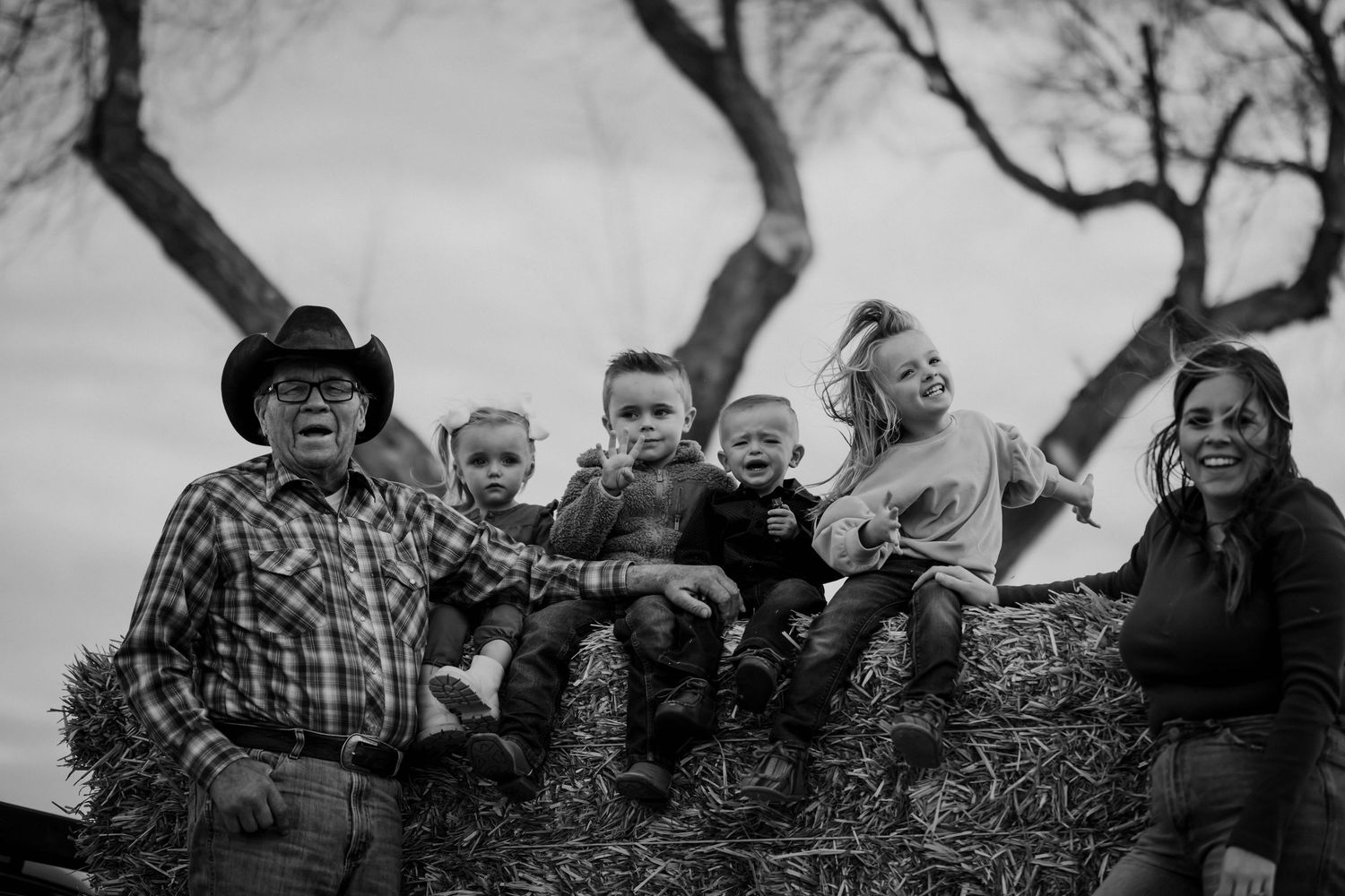 Black and white portrait of grandfather in cowboy hat with grandchildren on hay bale.