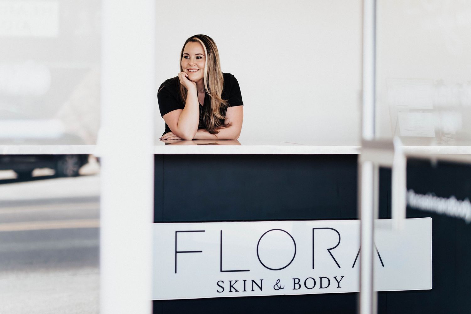 Woman smiling behind a white reception desk at Flora Skin and Body salon.