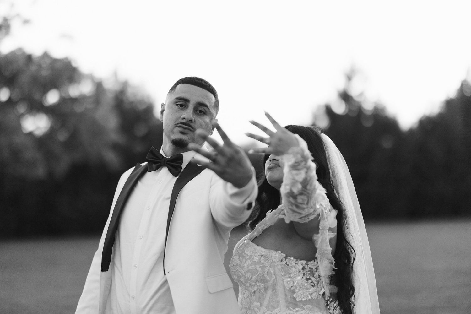 Black and white wedding photo of bride and groom showing rings outdoors.