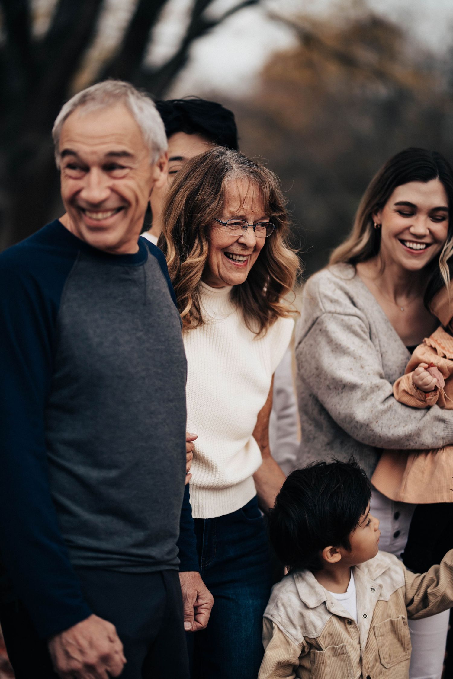 Multi-generational family walking and smiling together in an autumn park with fallen leaves.
