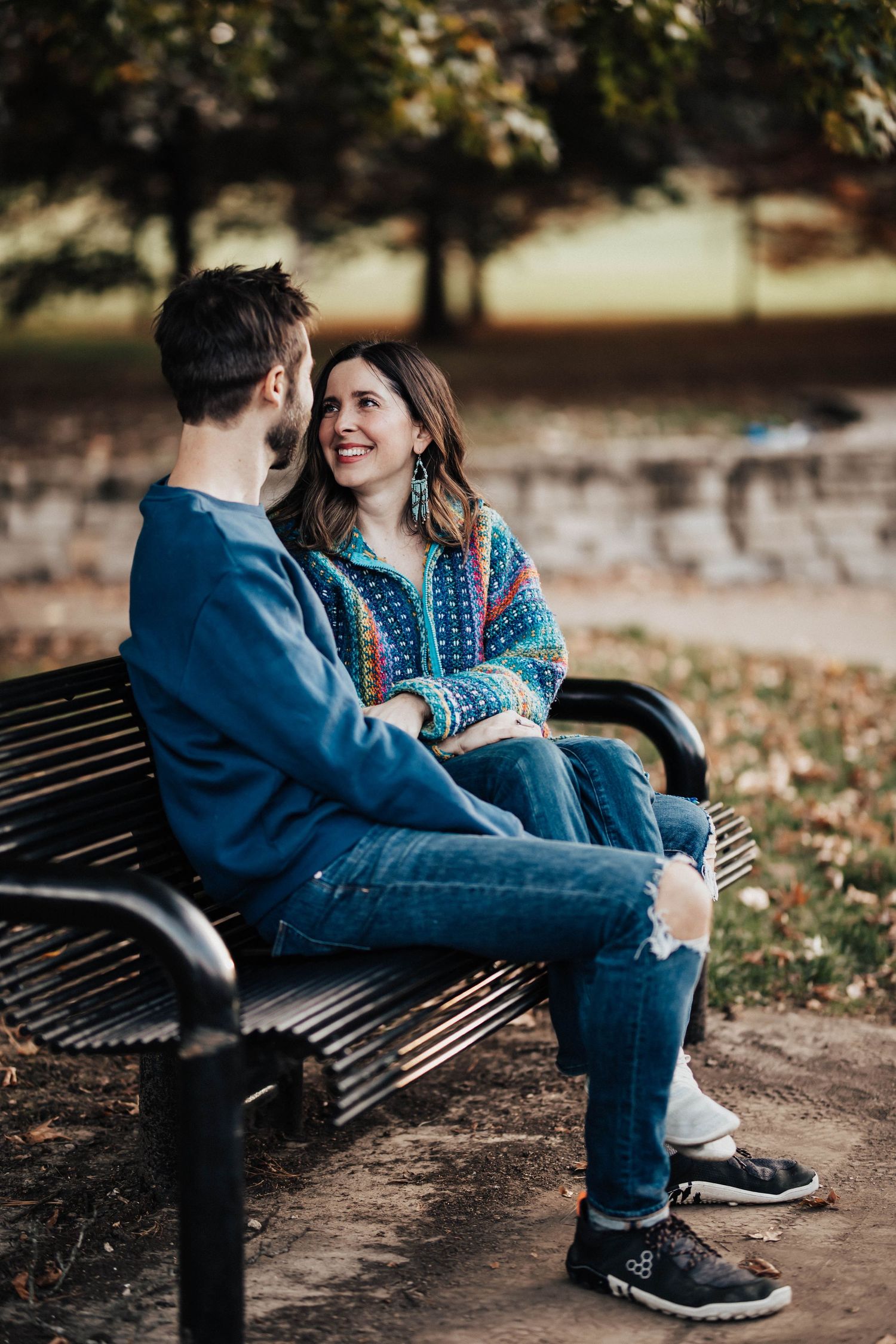 Happy couple sitting close together on a park bench in autumn, woman in colorful jacket smiling.