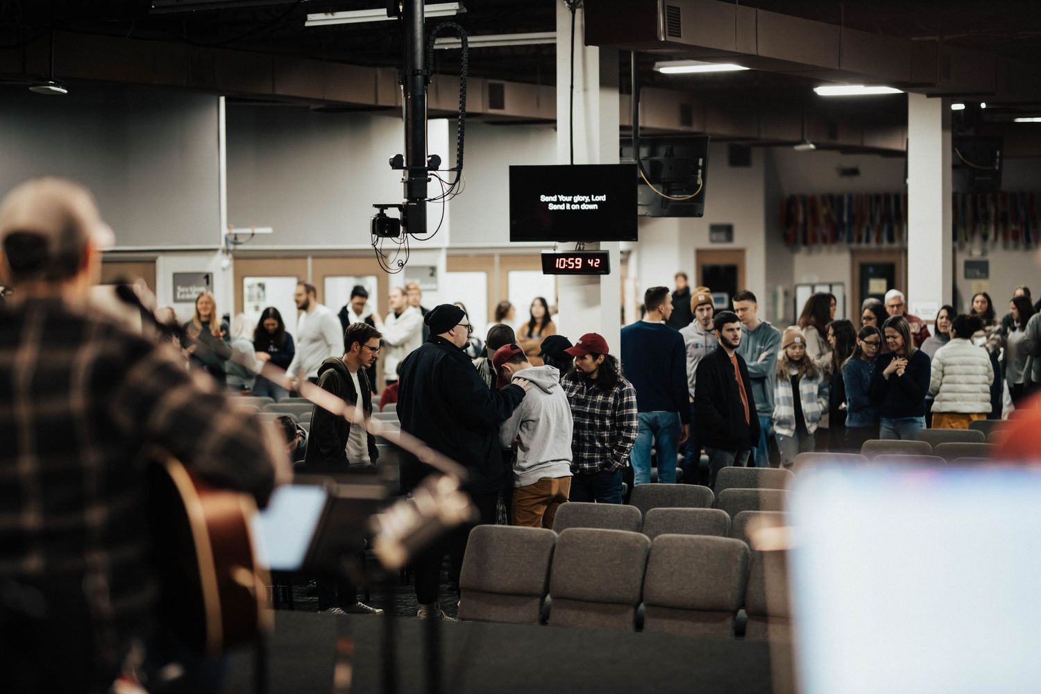 Congregation gathered in a modern church hall during a worship service with a guitarist performing on stage.