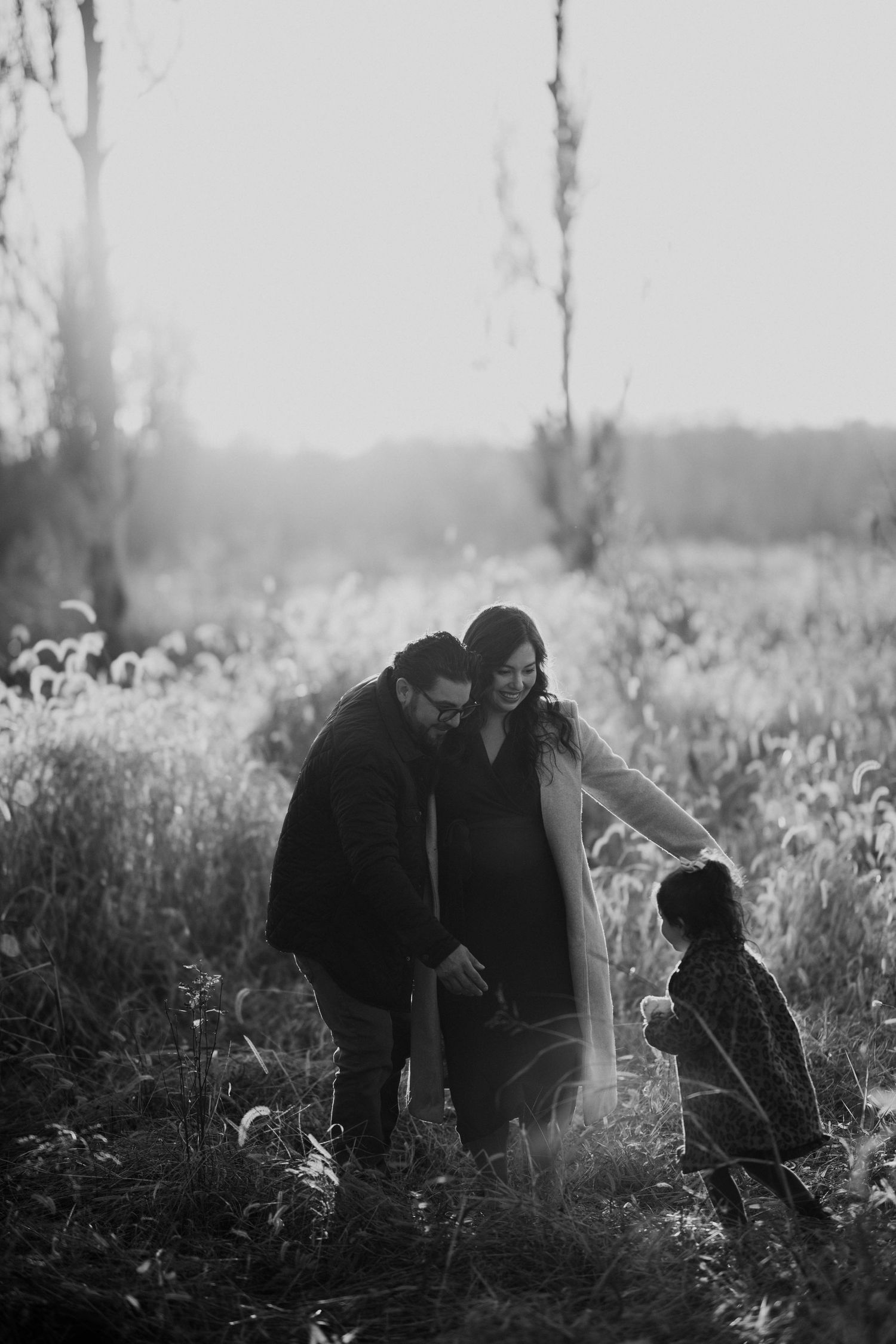 Black and white photo of a family with child in a sunlit field at dusk.