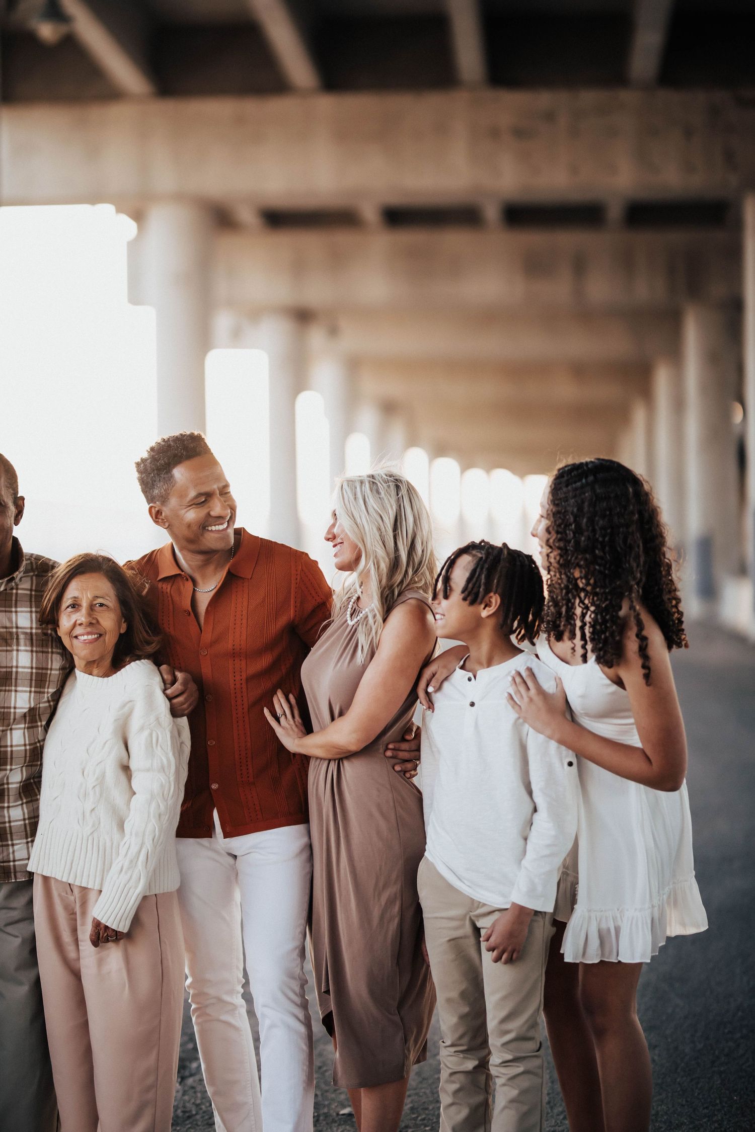 Multi-generational family smiling and embracing under concrete pillars in warm autumn tones.