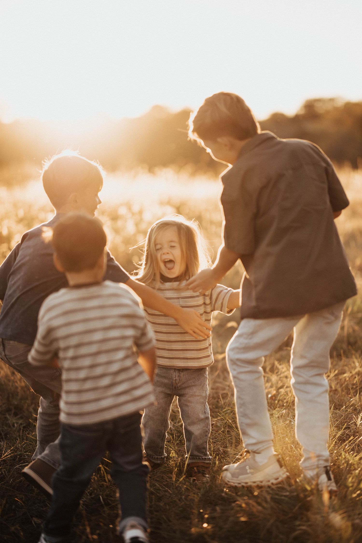Three children laughing and playing together in a sunlit field at golden hour.
