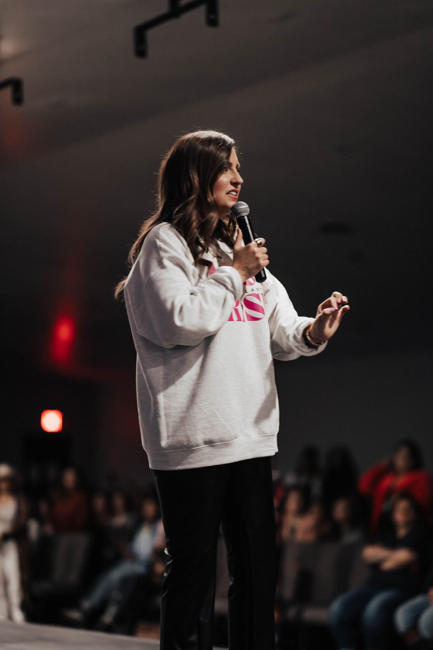 A woman in a white sweatshirt speaks into a microphone on stage at a conference.