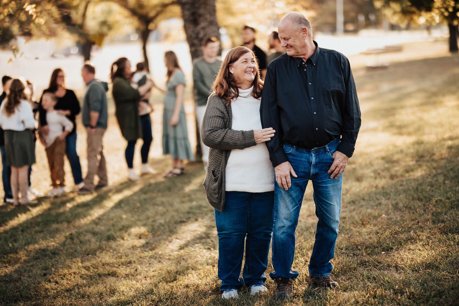 Grandparents sharing a tender moment outdoors with family gathered in golden autumn light.