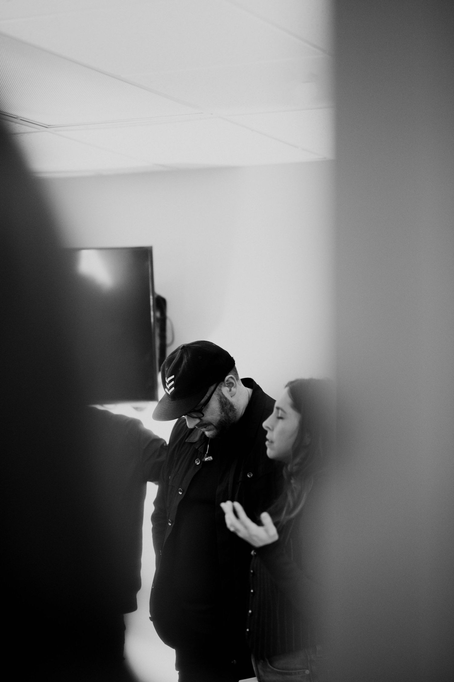 Black and white photo of a couple sharing an intimate moment, man in beanie and jacket leaning toward woman indoors.