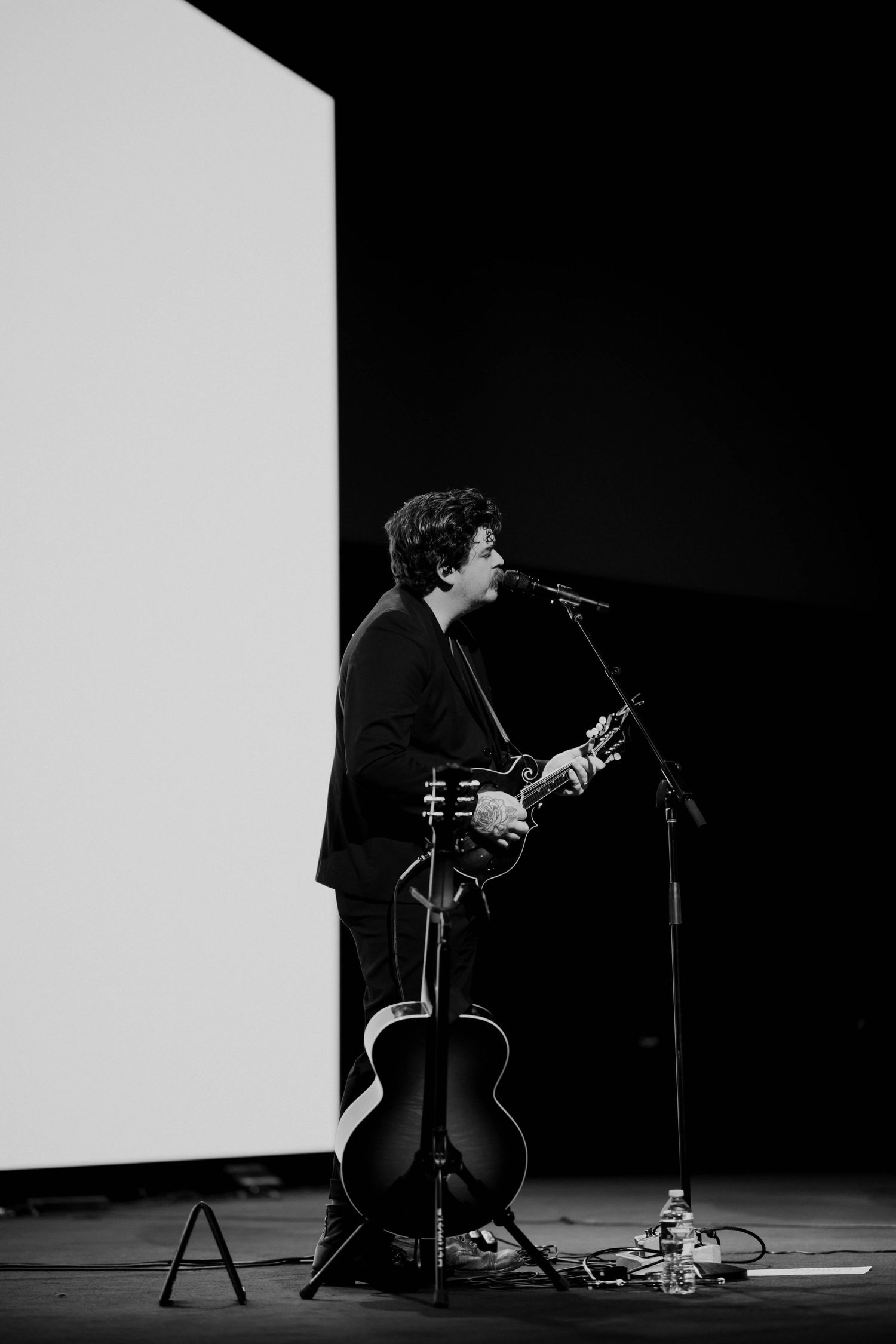 Black and white photo of a guitarist singing at a microphone on stage.